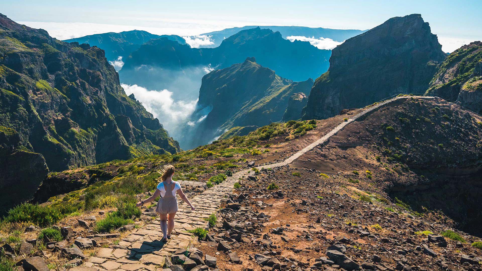 Mujer caminando por un sendero en las montañas con nubes en Madeira.