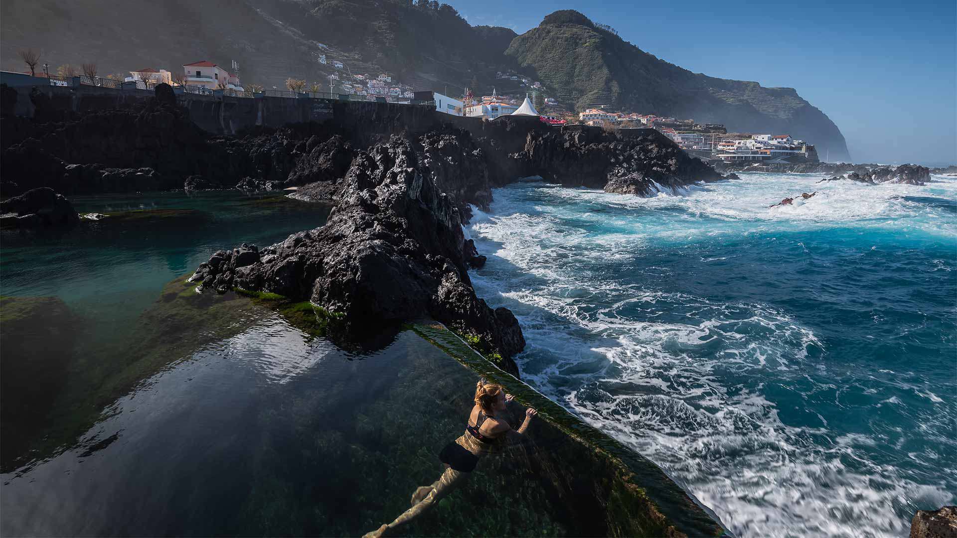 Person in einem Naturpool blickt auf das Meer und die Felslandschaft Madeiras.