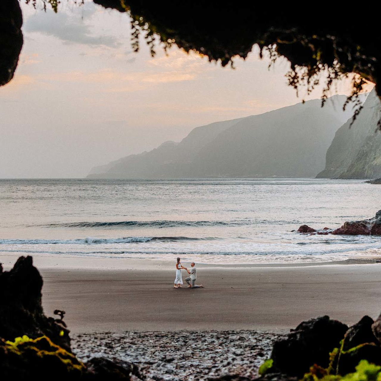 Casal ao fundo na praia do Seixal, com rochas em primeiro plano.