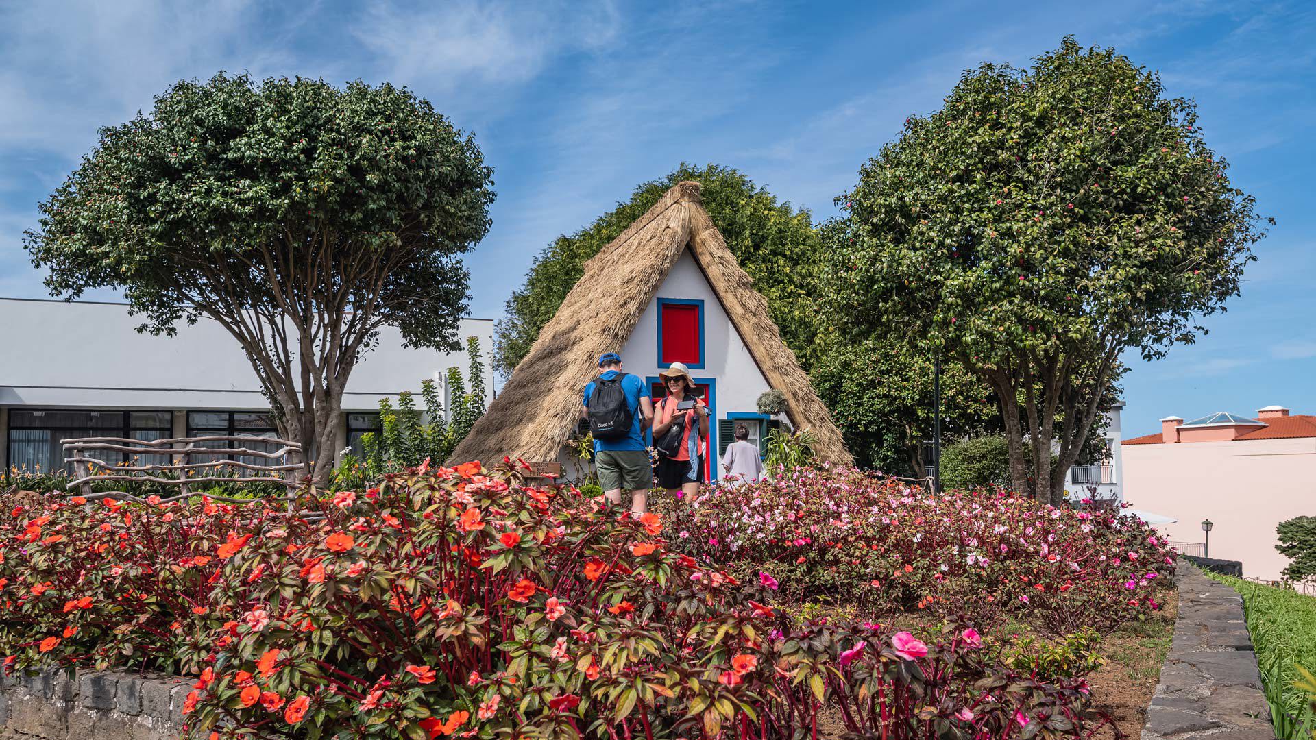 Maison triangulaire entourée d’arbres, jardin et fleurs rouges à Madère.