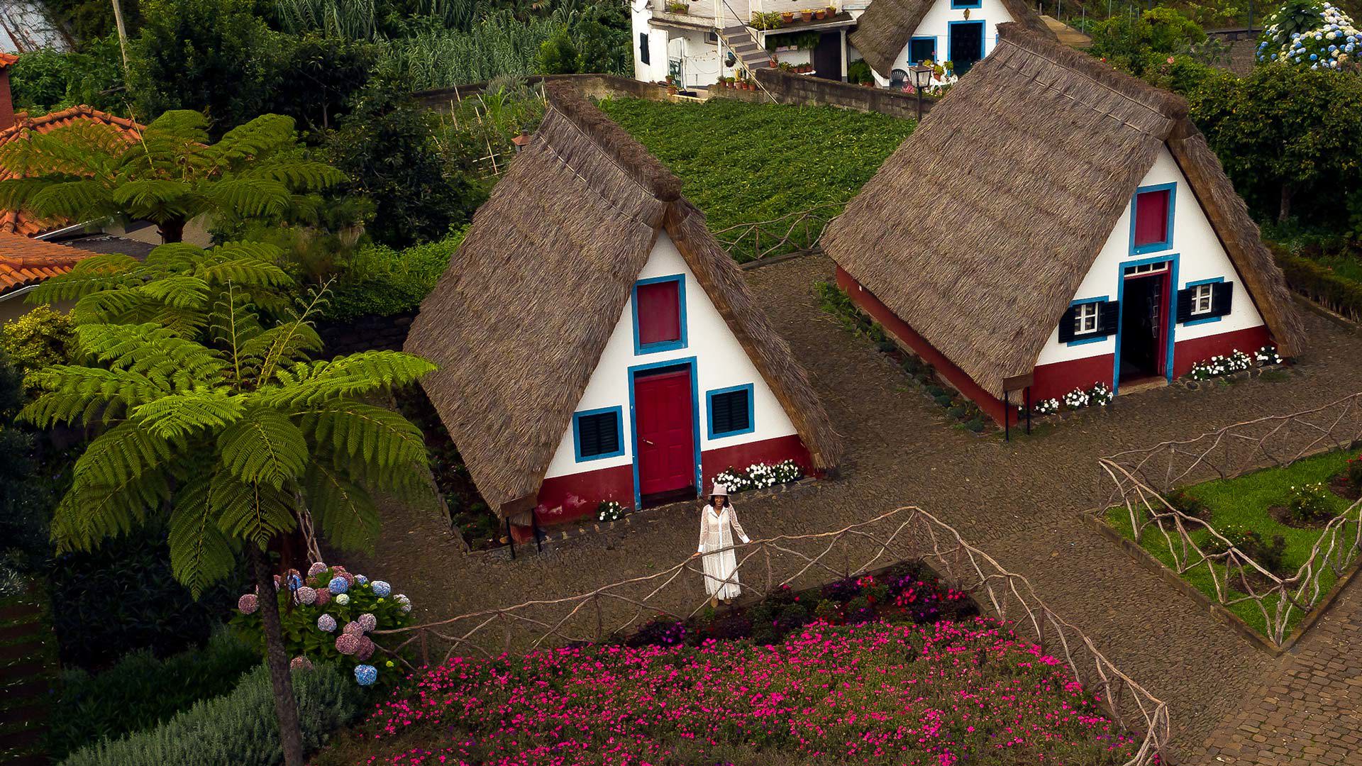 Femme en robe blanche près de maisons triangulaires aux toits de chaume.