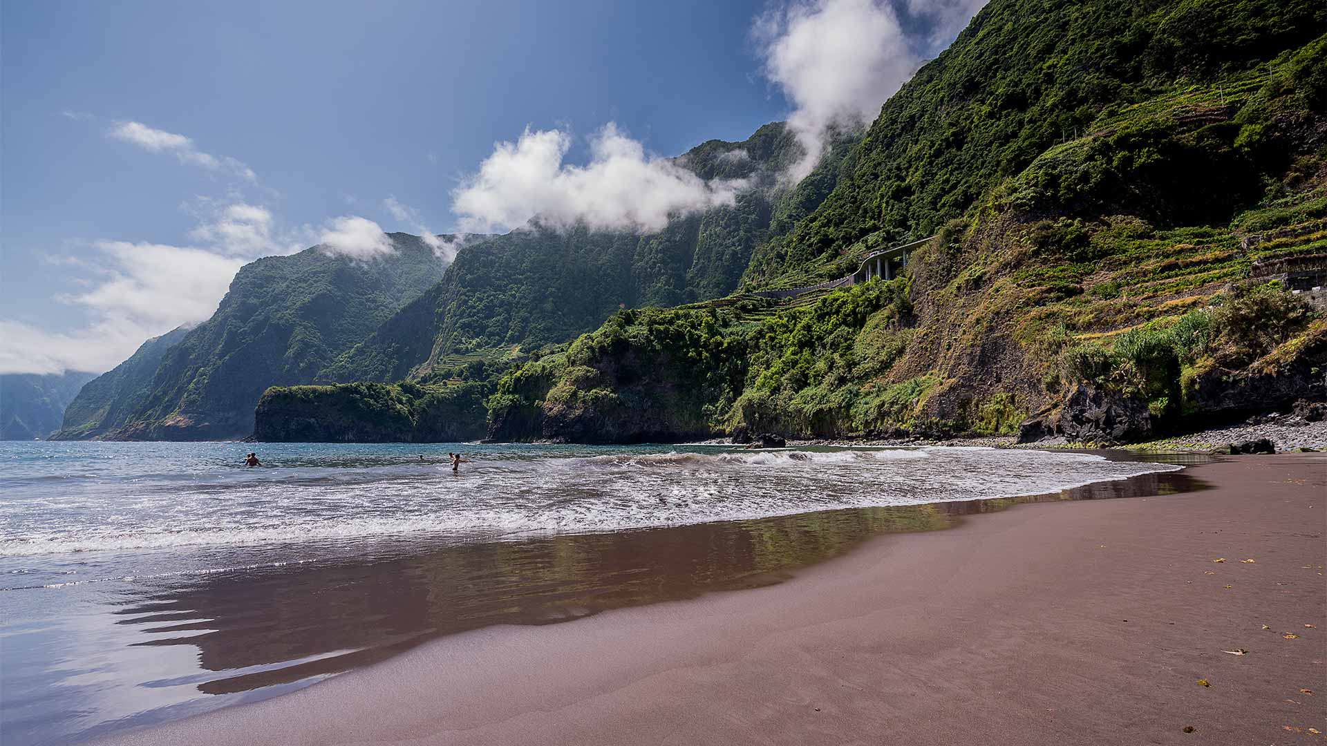 Black sand beach with sea and mountains in the background in Madeira.