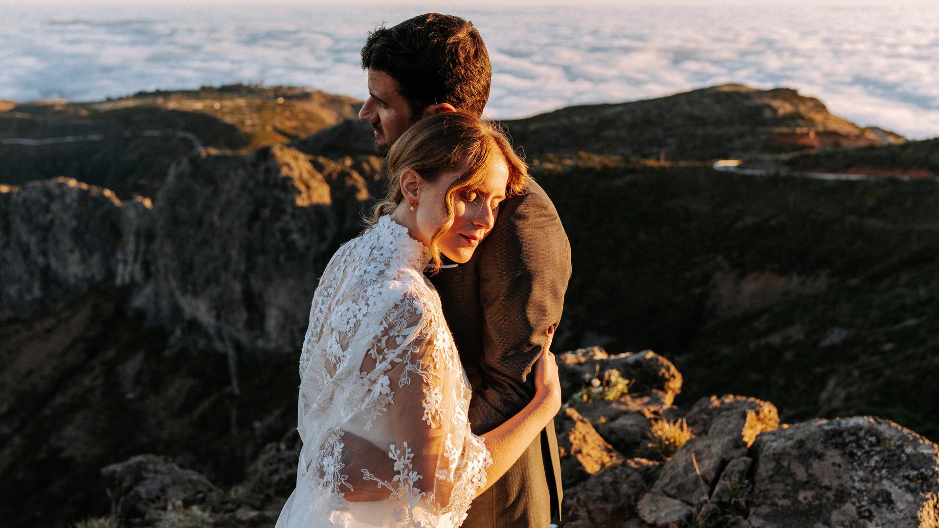 Casal em trajes de casamento nas montanhas, acima das nuvens, abraçados.