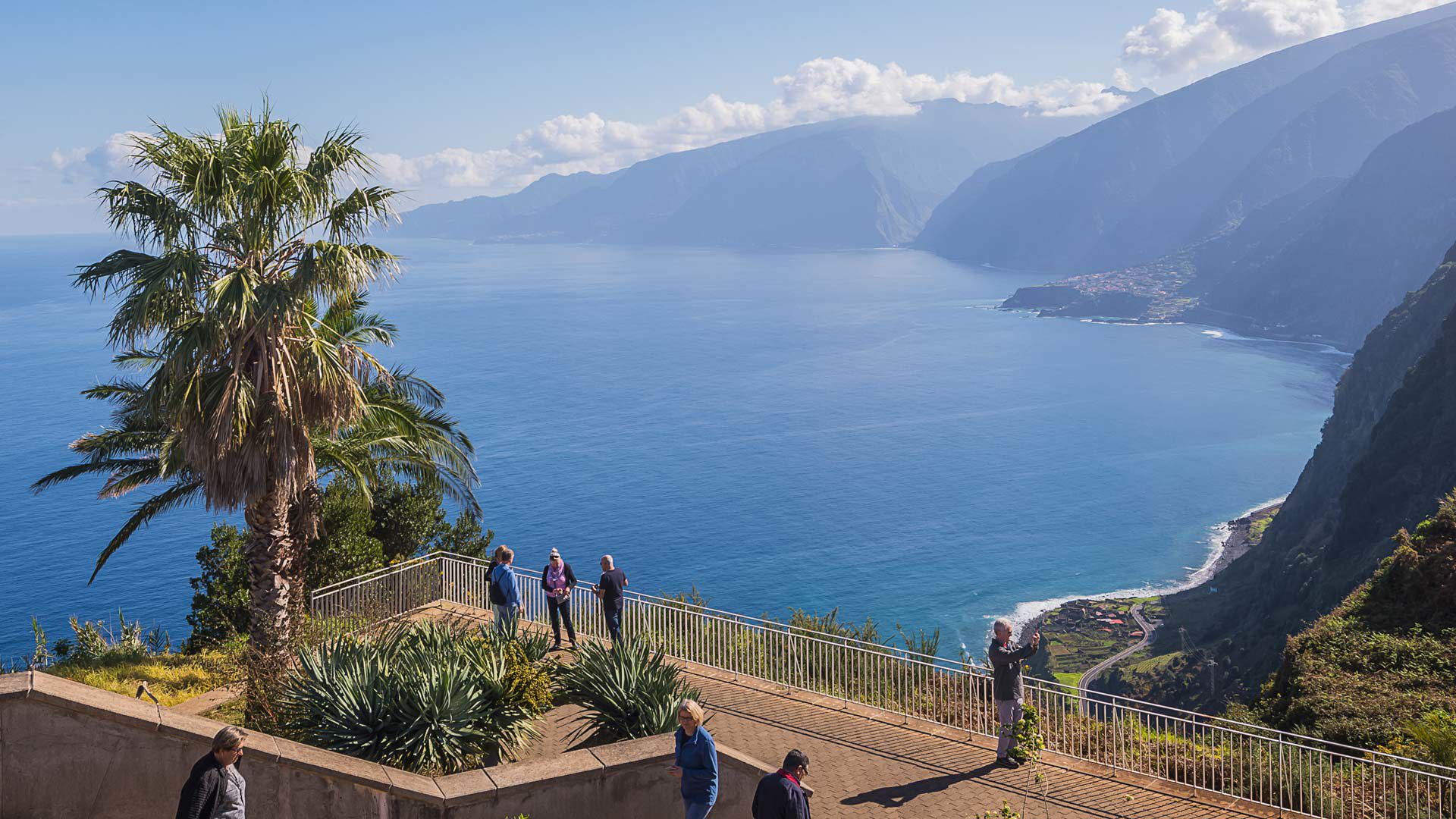Viewpoint with palm tree and people enjoying the coast and sea in Madeira.