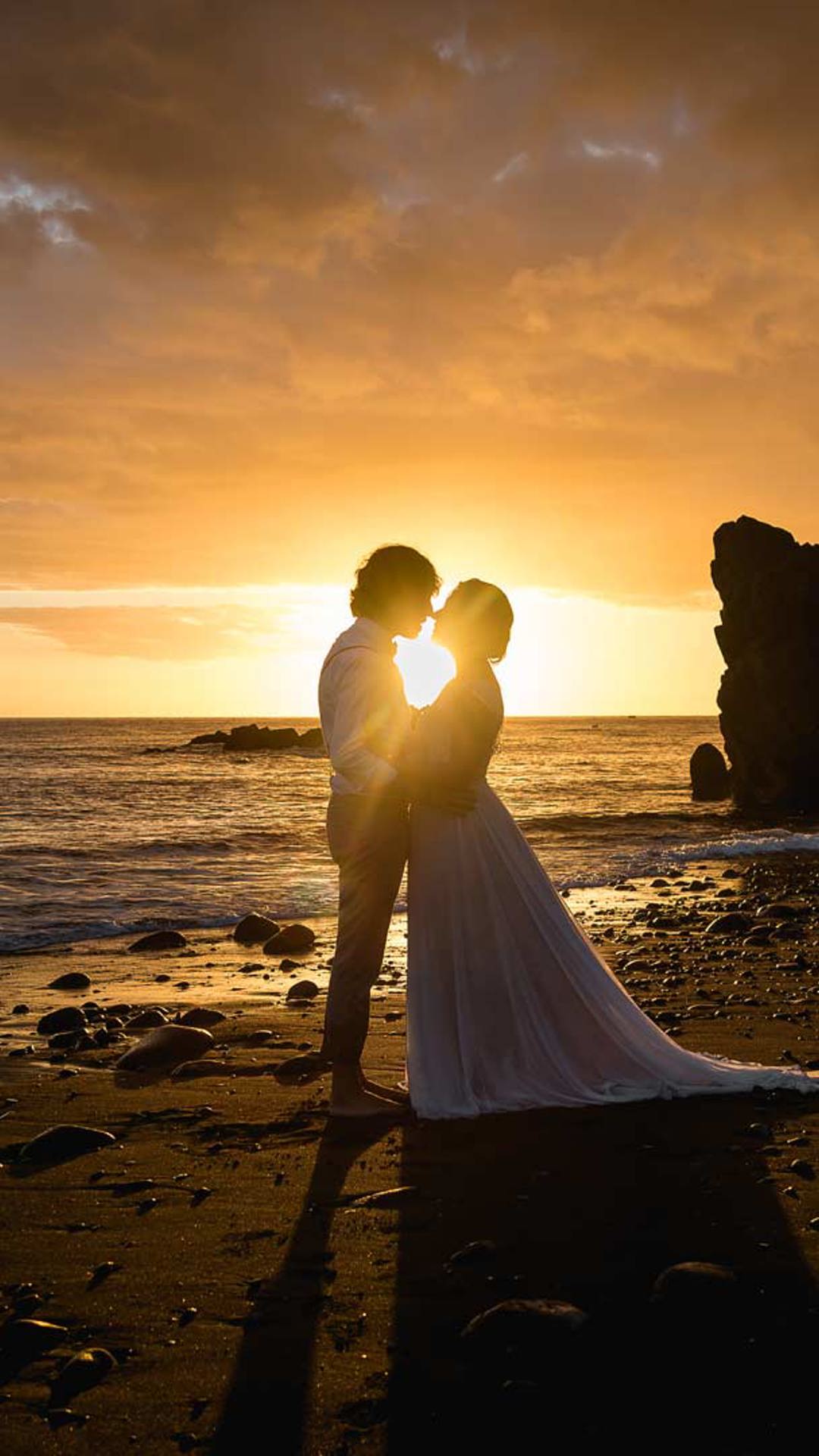 Pareja con atuendos de boda disfrutando del atardecer en la playa.
