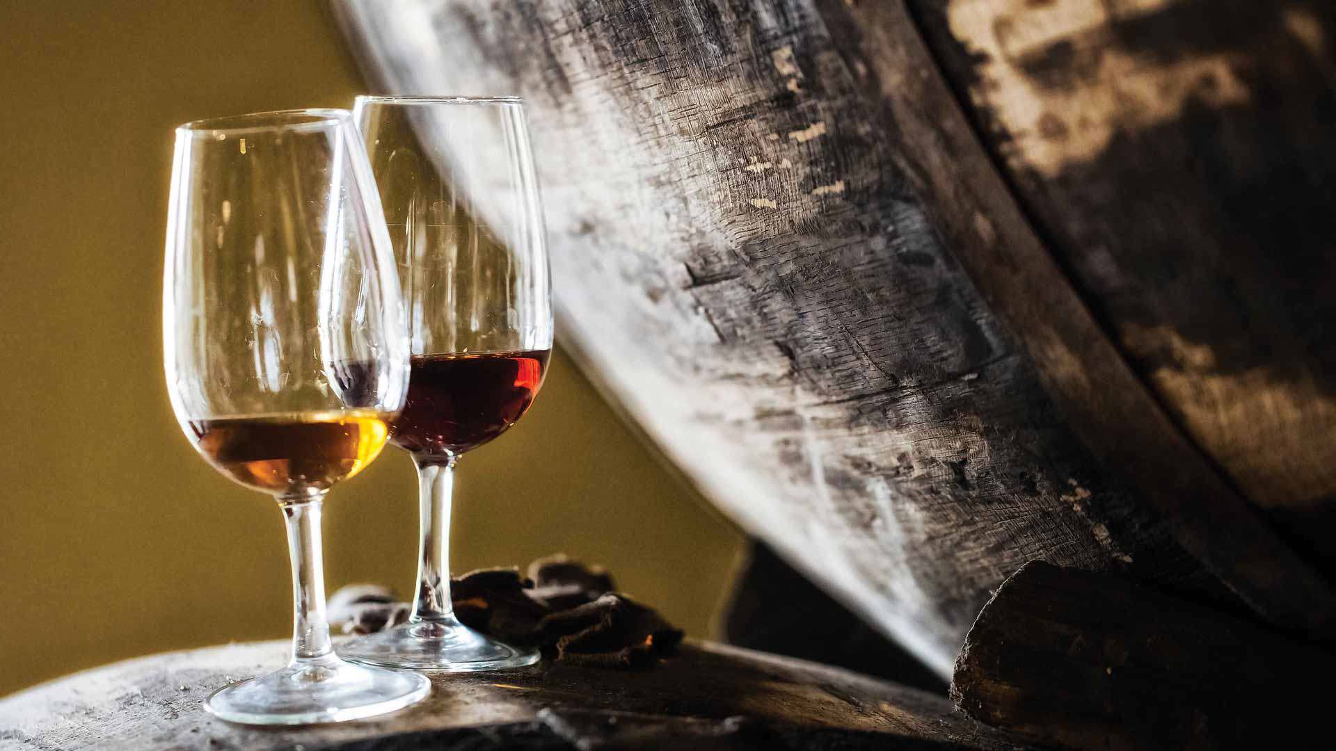 Two glasses of Madeira wine beside a wine barrel.