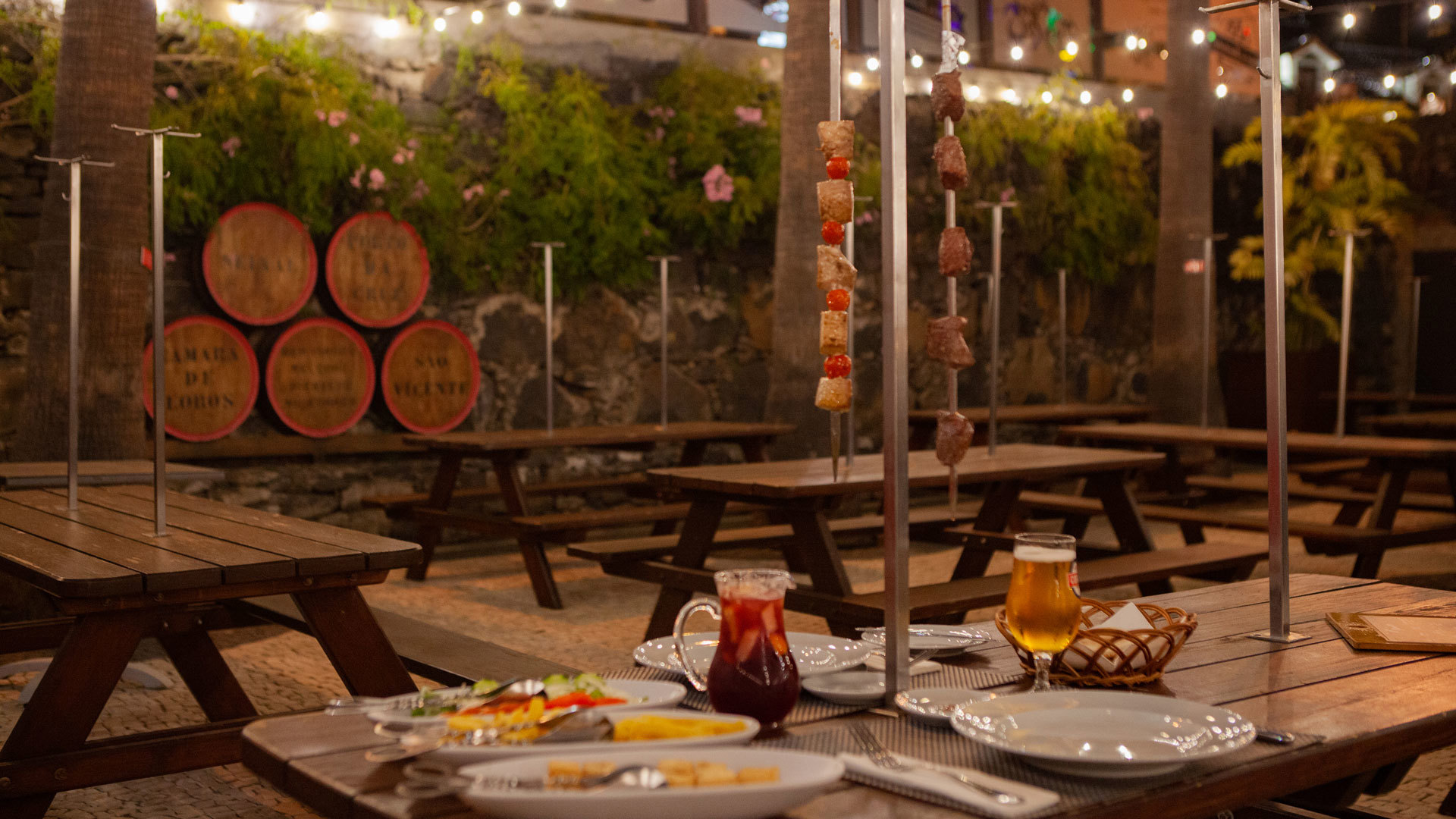 Table with skewers, pitchers of drinks, and plates of food.