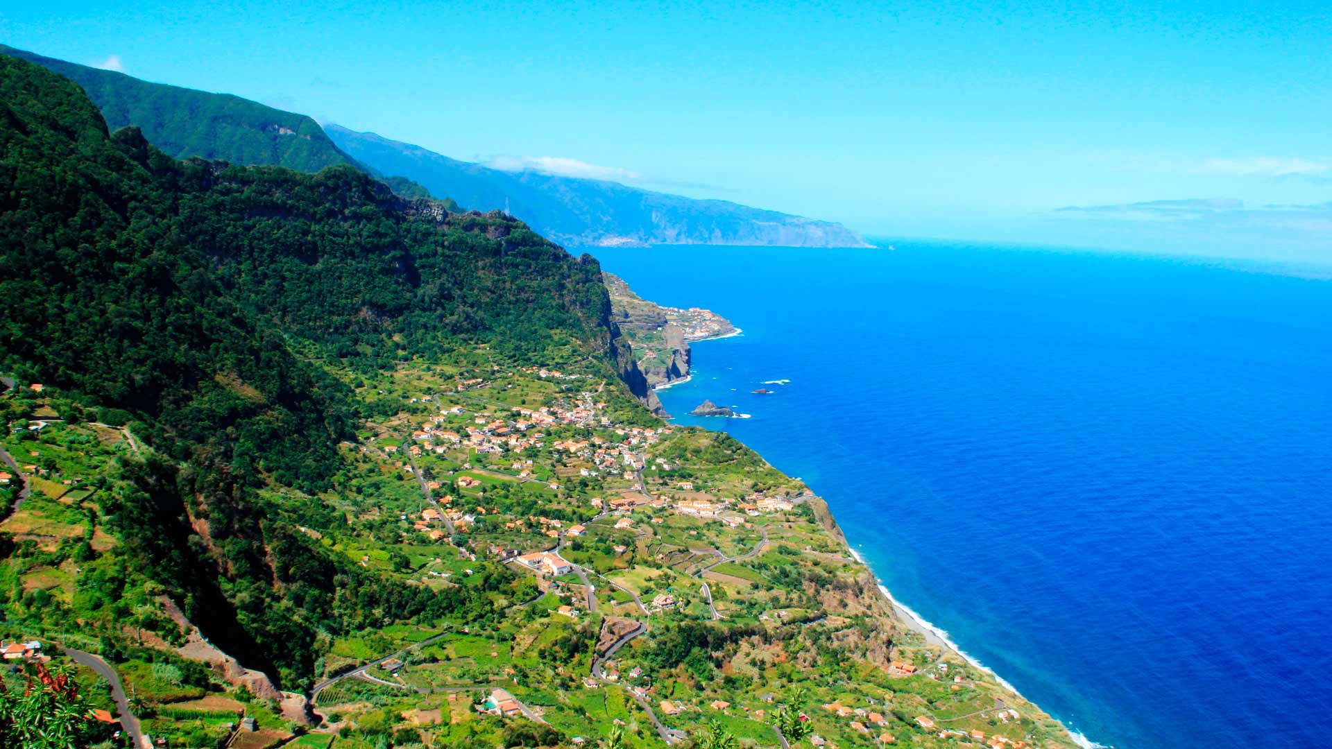 Grüne Hanglage mit Häusern direkt am Meer auf Madeira.