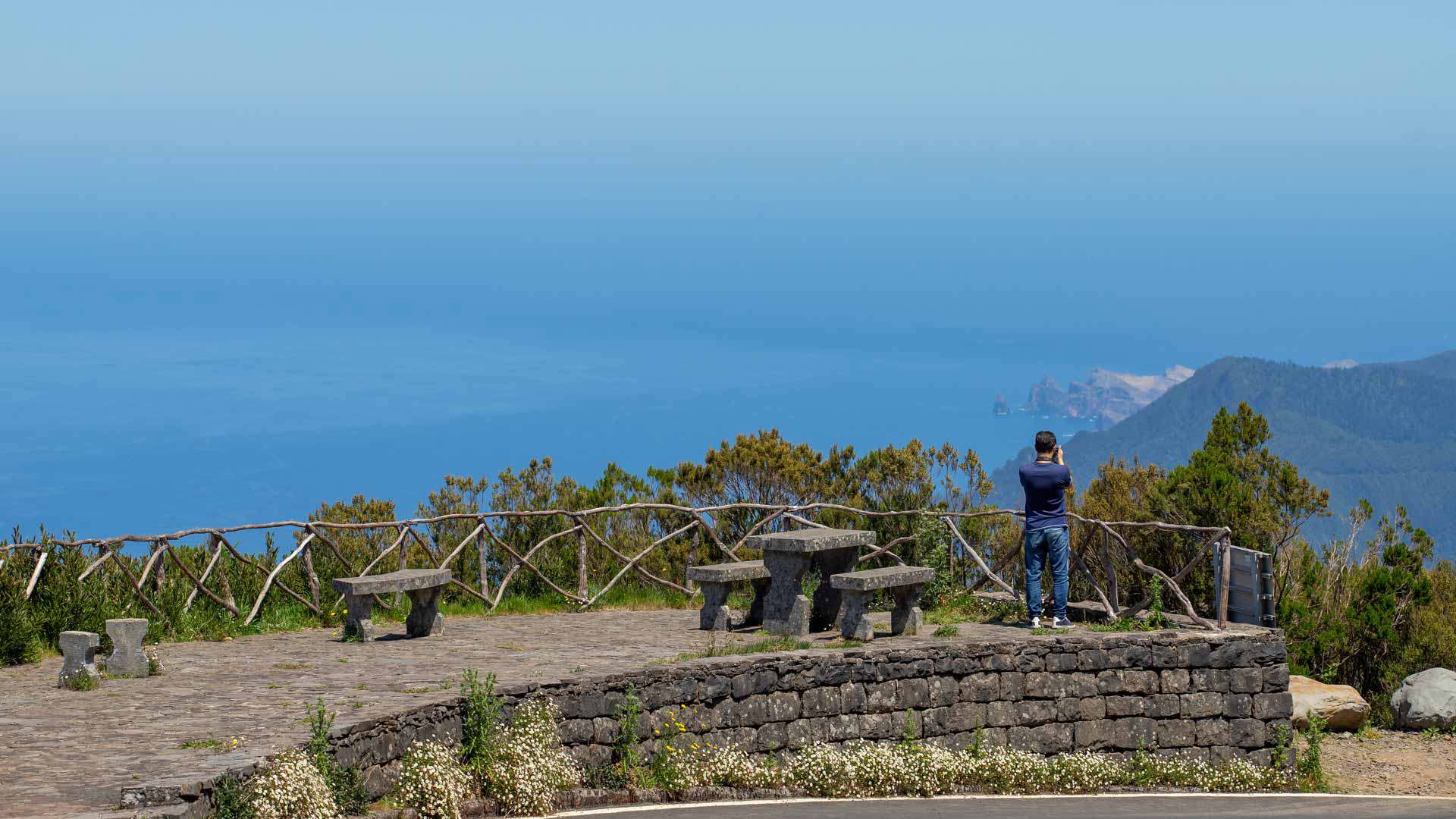 Person am Stein-Aussichtspunkt mit Blick auf Meer und Berge.