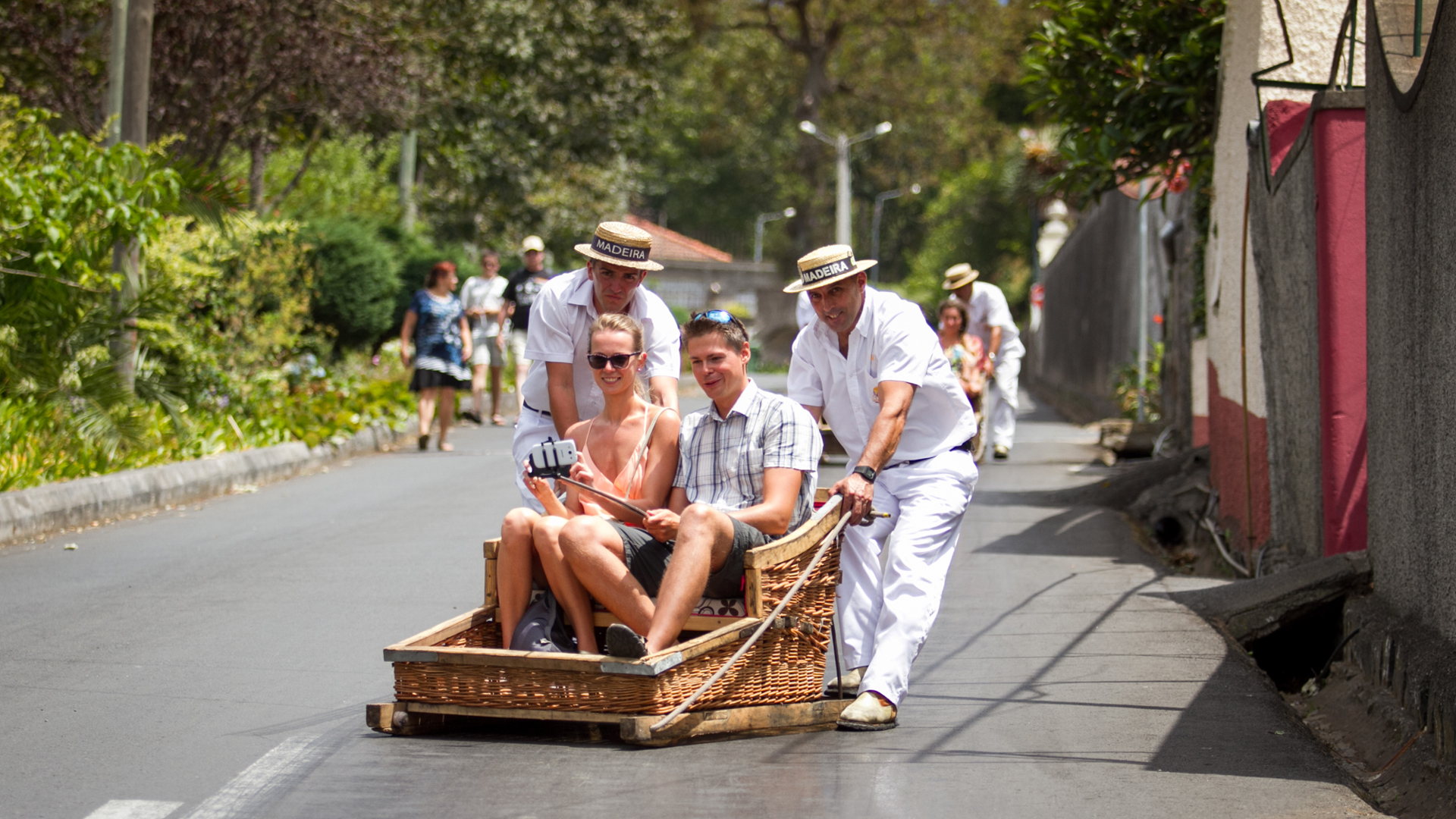 Carreiros pushing wicker sledges with people down the road in Madeira.