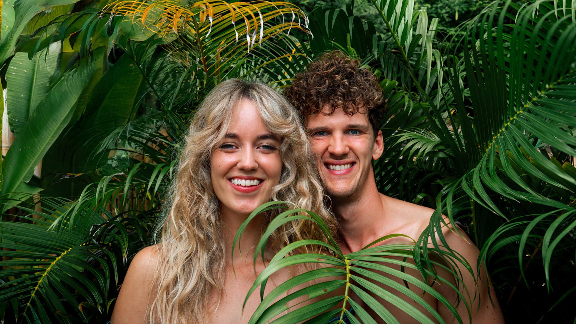 Paar lächelt, umgeben von Vegetation.