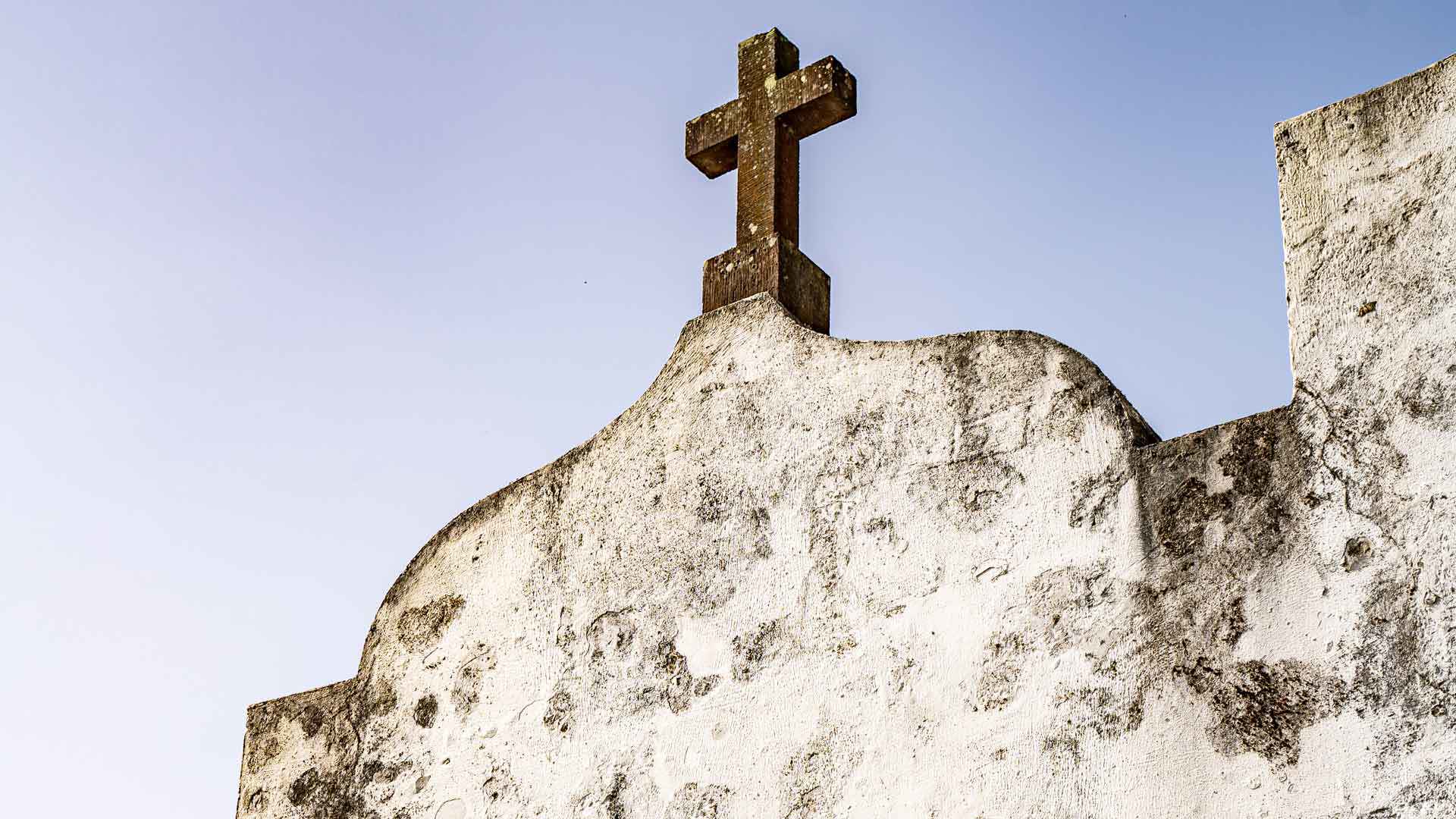 Cruz en la cima de capilla con cielo de fondo.