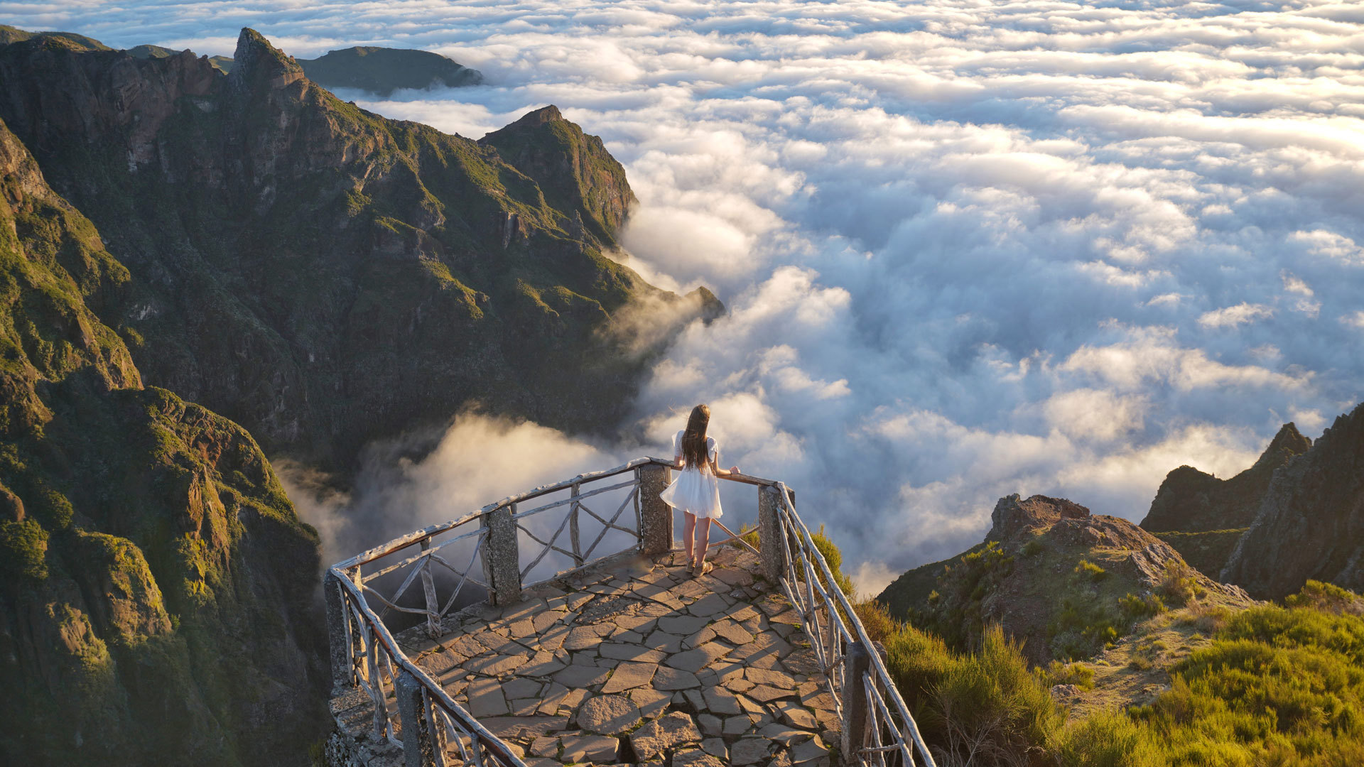 Woman in white dress at a viewpoint with clouds in the background in Madeira.