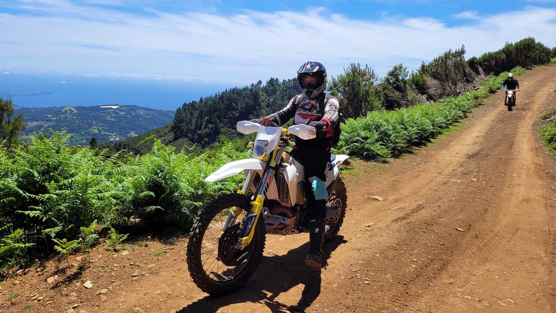 Person riding a dirt bike on an enduro trail, surrounded by landscape.