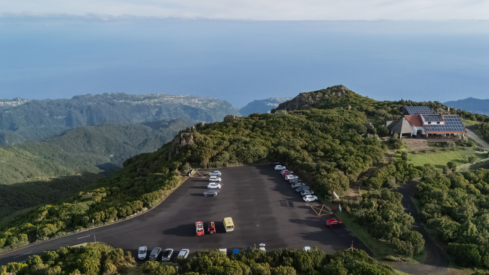 Car parking area with trees and sea in the background.