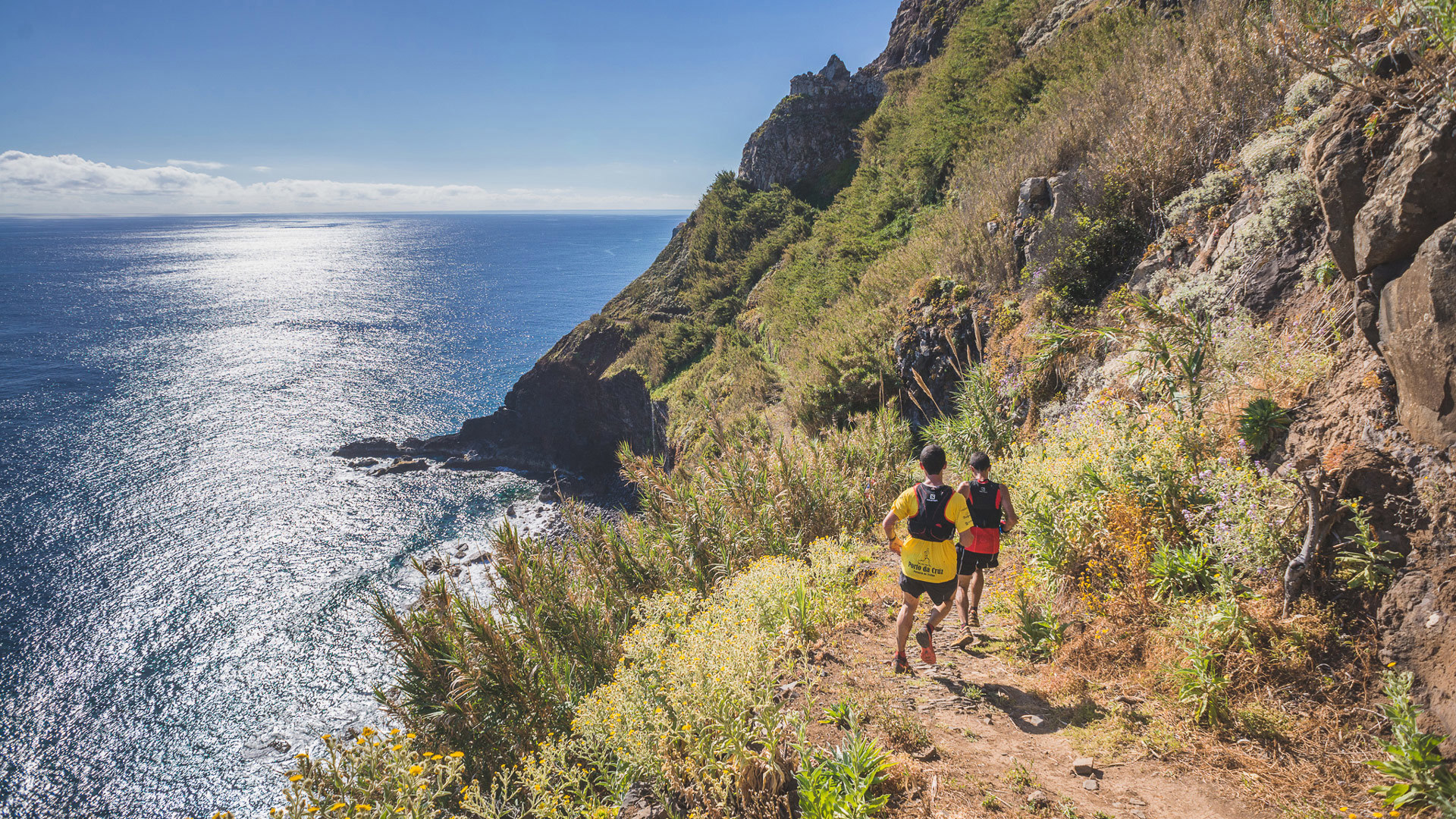 Duas pessoas a correr em trilho na montanha com o mar ao largo.