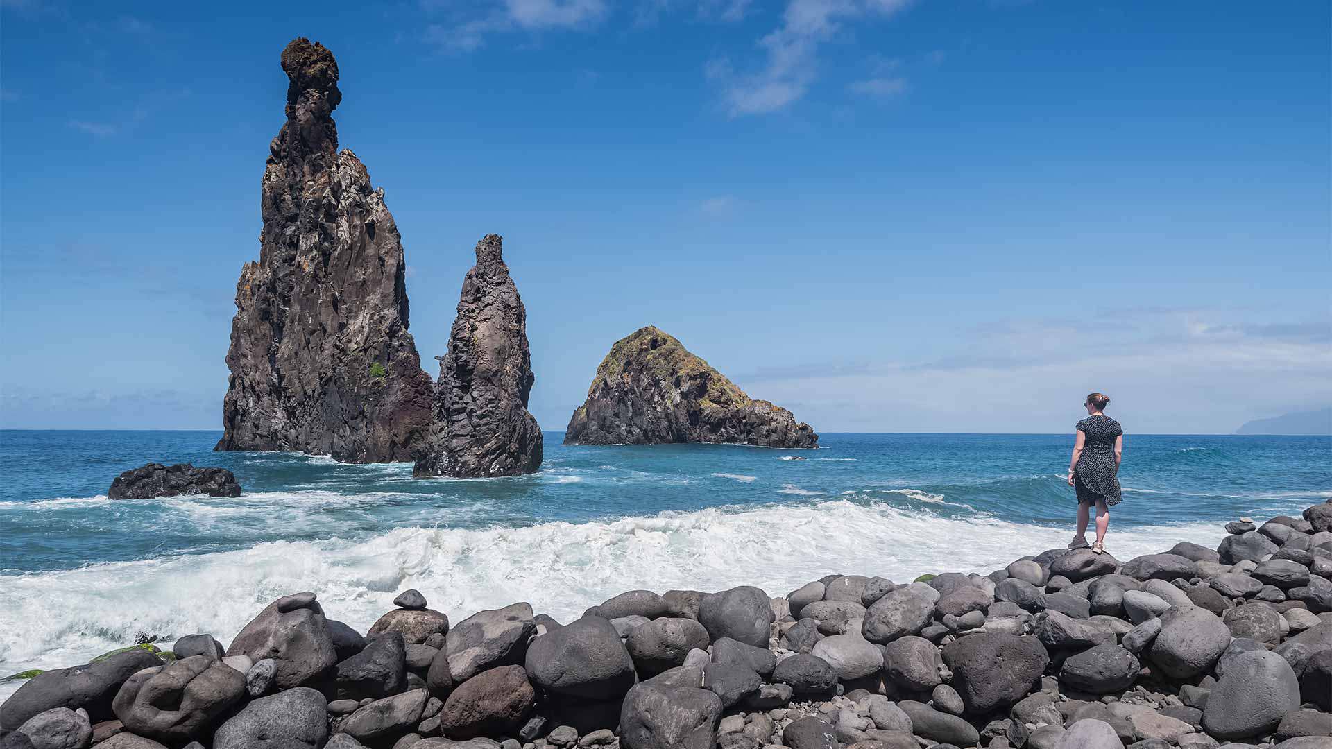 Mulher junto a formação rochosa e pedras à beira-mar na Madeira.