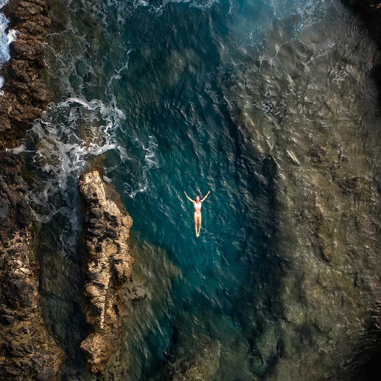 Woman at the natural pools of Porto Moniz by the sea and rocks.