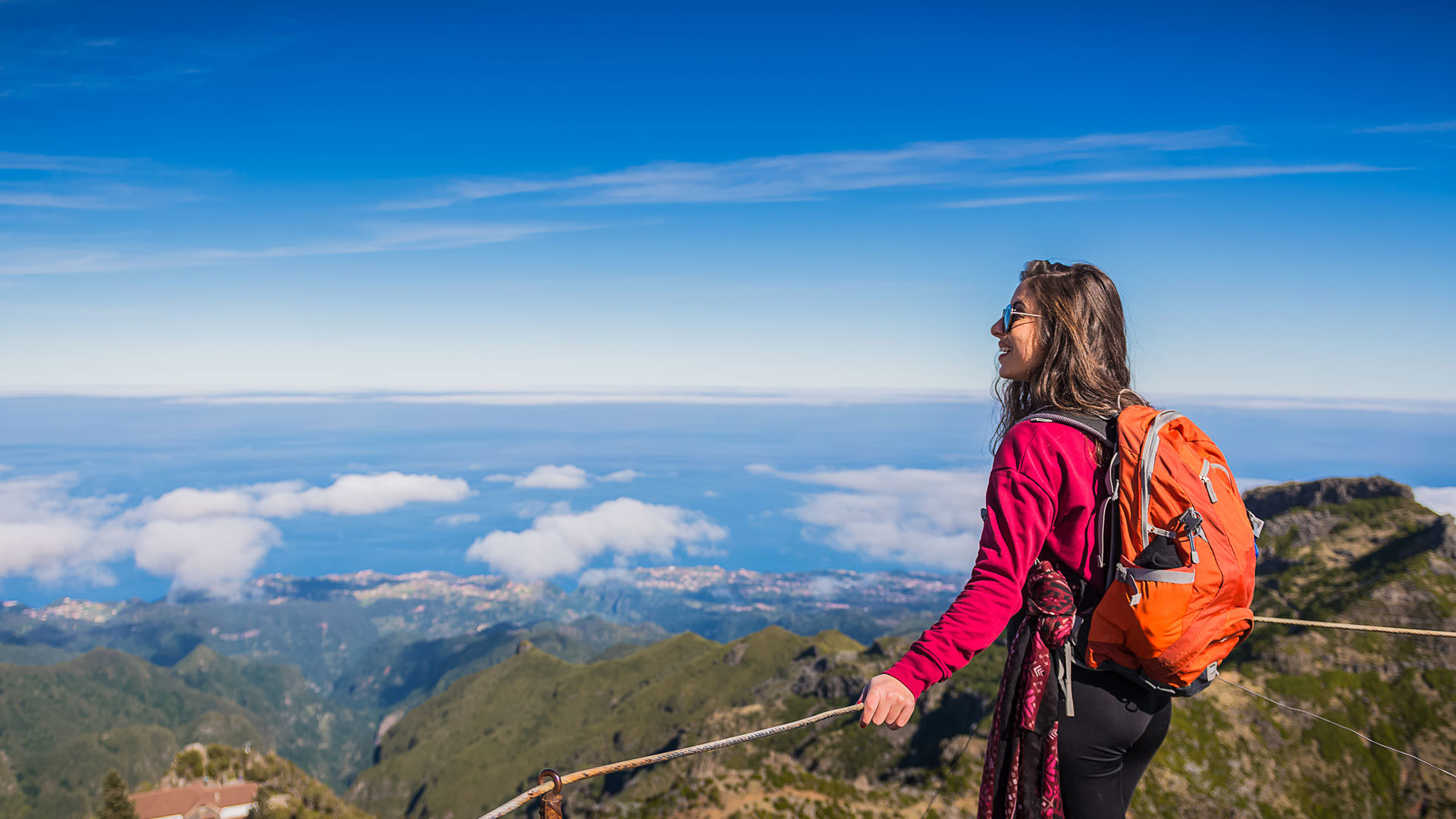 Mujer con chaqueta rosa y mochila naranja en un mirador en Madeira.