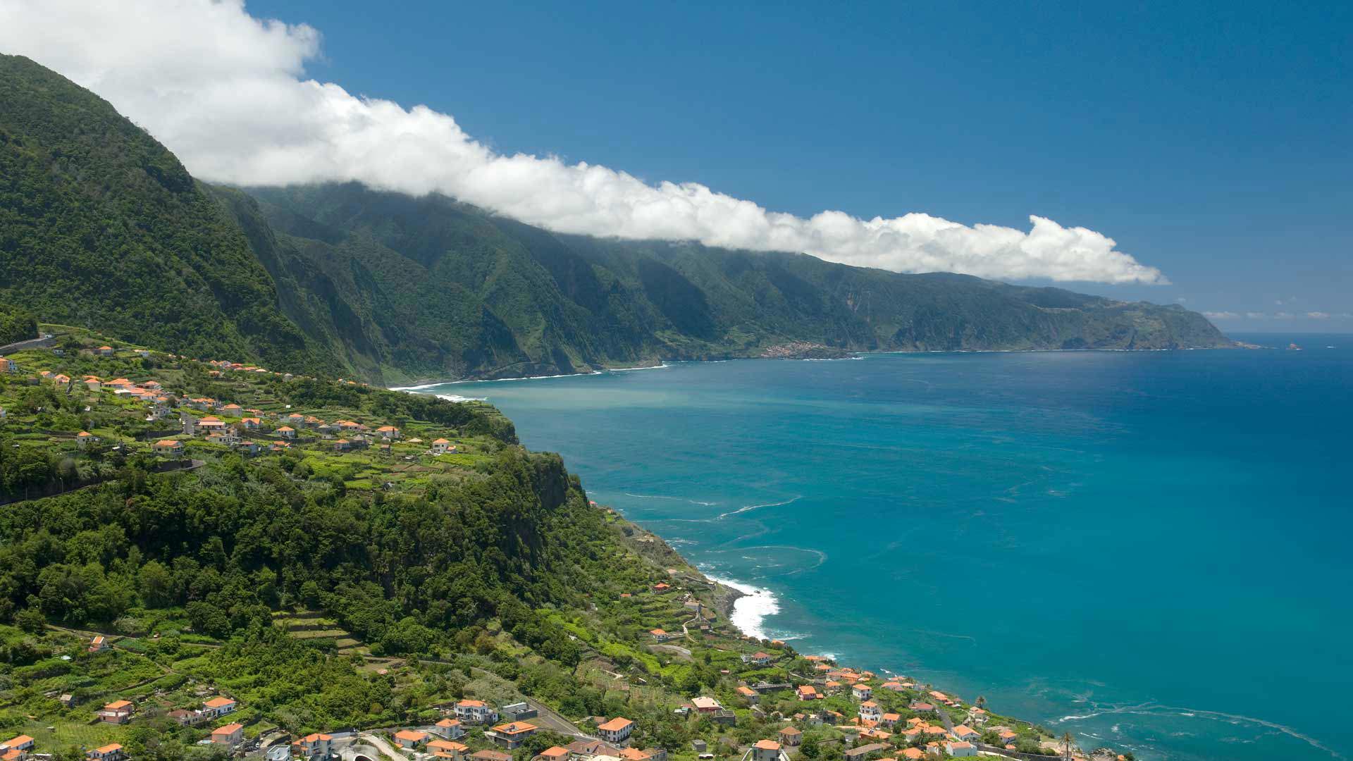 Paisagem de natureza com montanha, mar e nuvens ao fundo.
