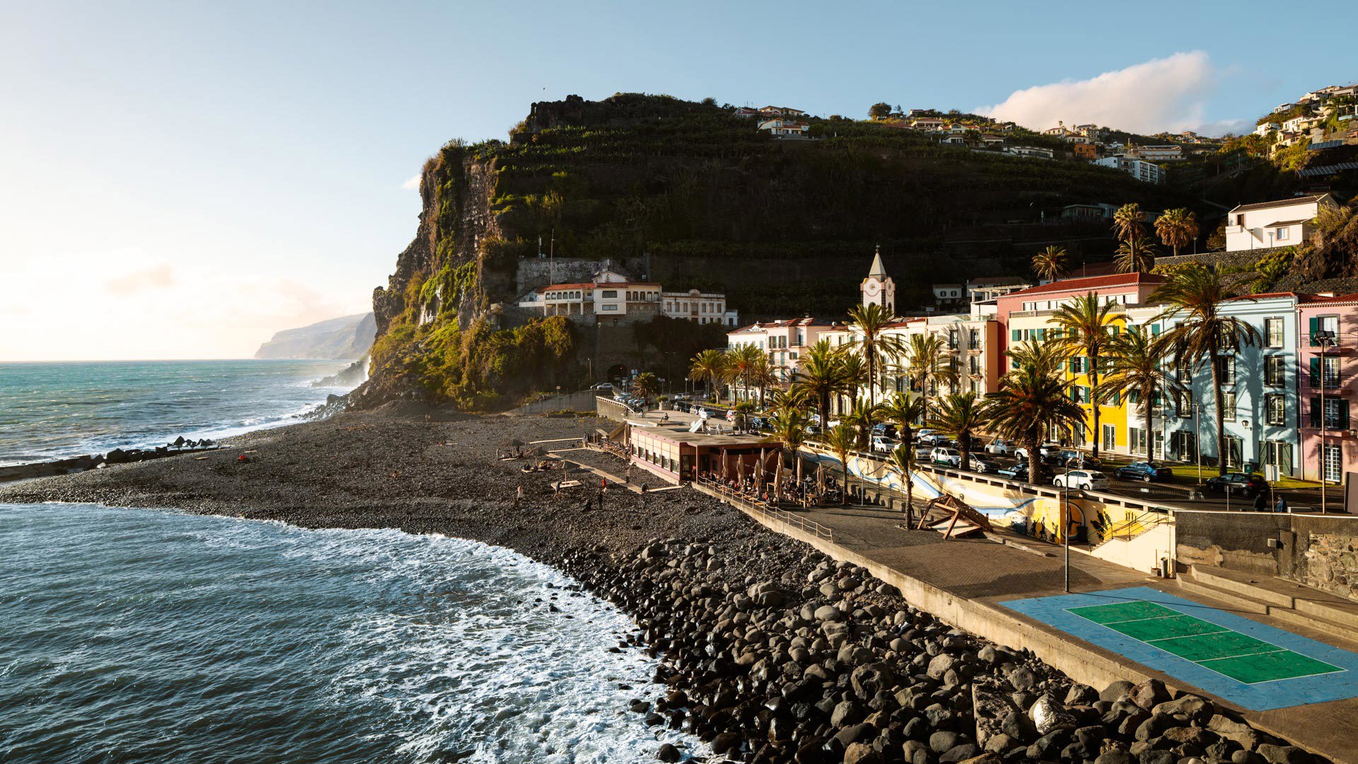 Kiesstrand in Ponta do Sol, mit Meer, bunten Gebäuden und Madeira-Hang.