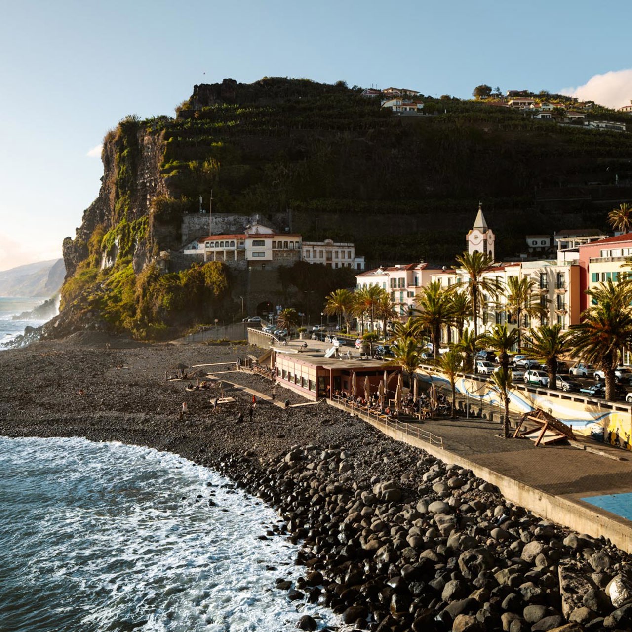 Kiesstrand in Ponta do Sol, mit Meer, bunten Gebäuden und Madeira-Hang.
