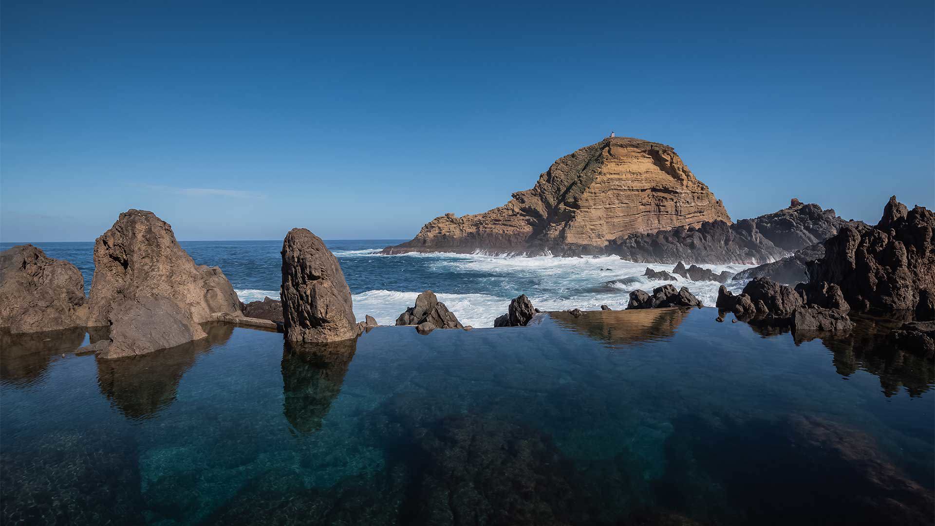 Naturpool am Meer zwischen Felsen, mit einem großen Felsen im Vordergrund.