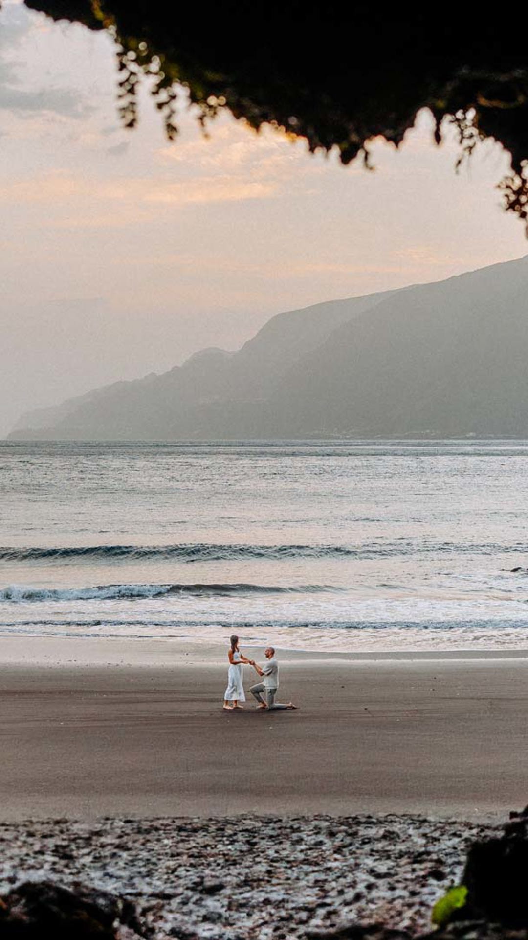 Pareja al fondo en la playa de Seixal, con rocas en primer plano.
