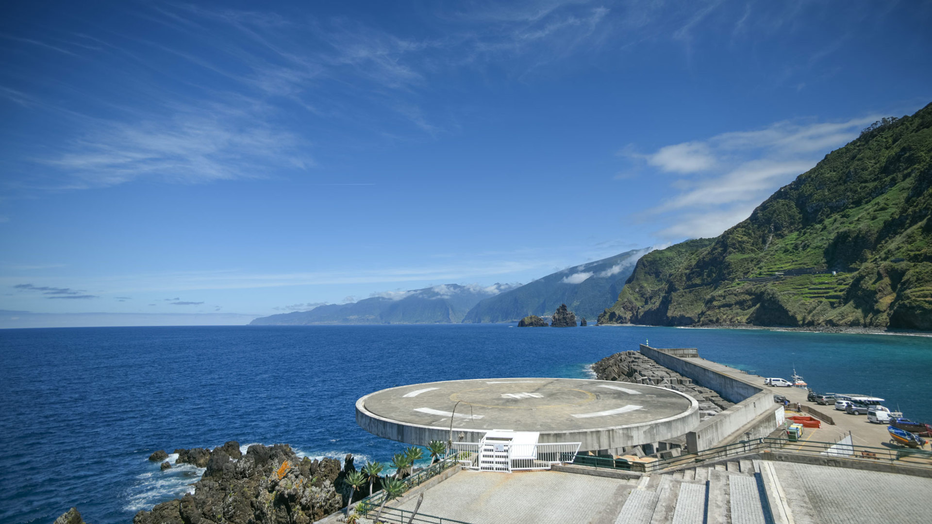Helipad by the sea and lush hillside.