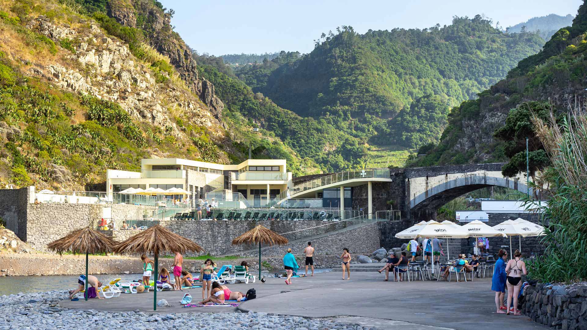 Personnes avec parasols sur la plage de galets près des montagnes de Madère.