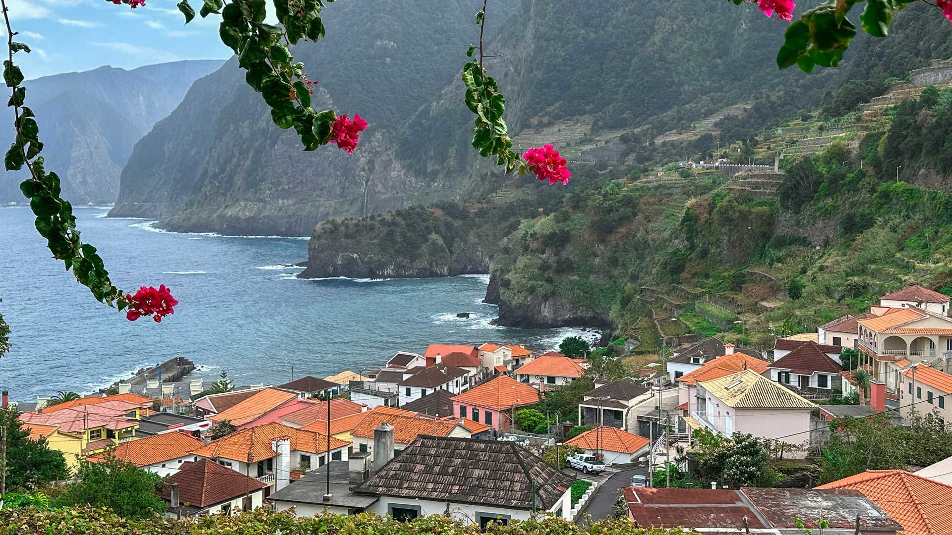Paisaje de Madeira con montañas, ladera, casas y el mar al fondo.