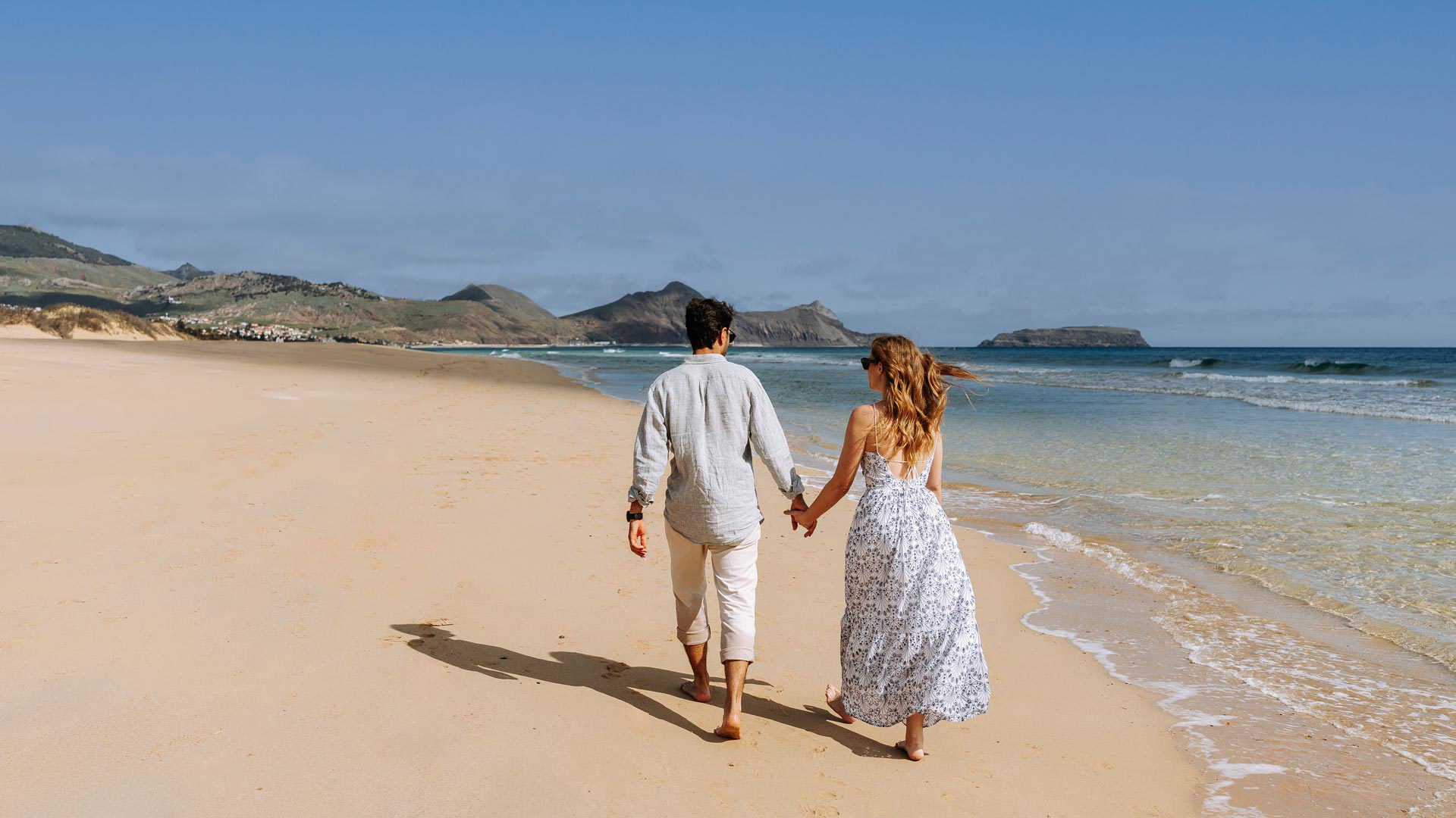 Pareja de espaldas caminando en la playa junto a la orilla del mar en Porto Santo.