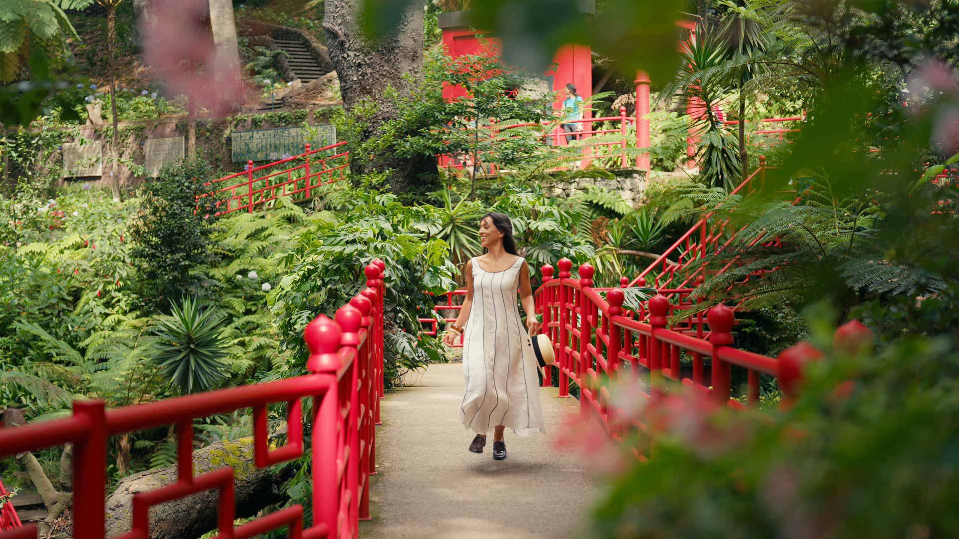 Femme traversant un pont oriental au Jardin Tropical Monte Palace Madeira entourée de végétation.