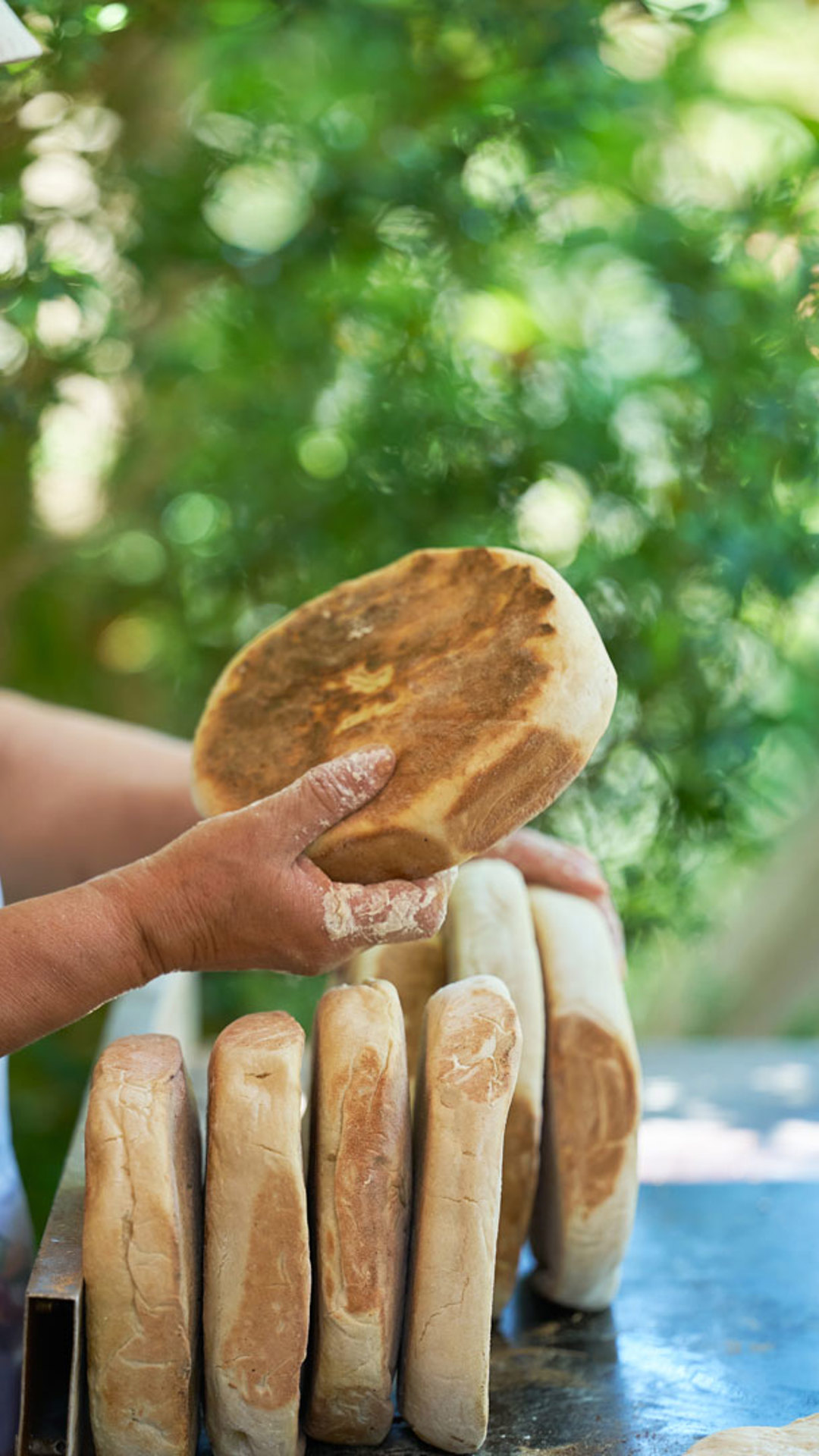 Woman preparing bolo do caco on a traditional griddle.