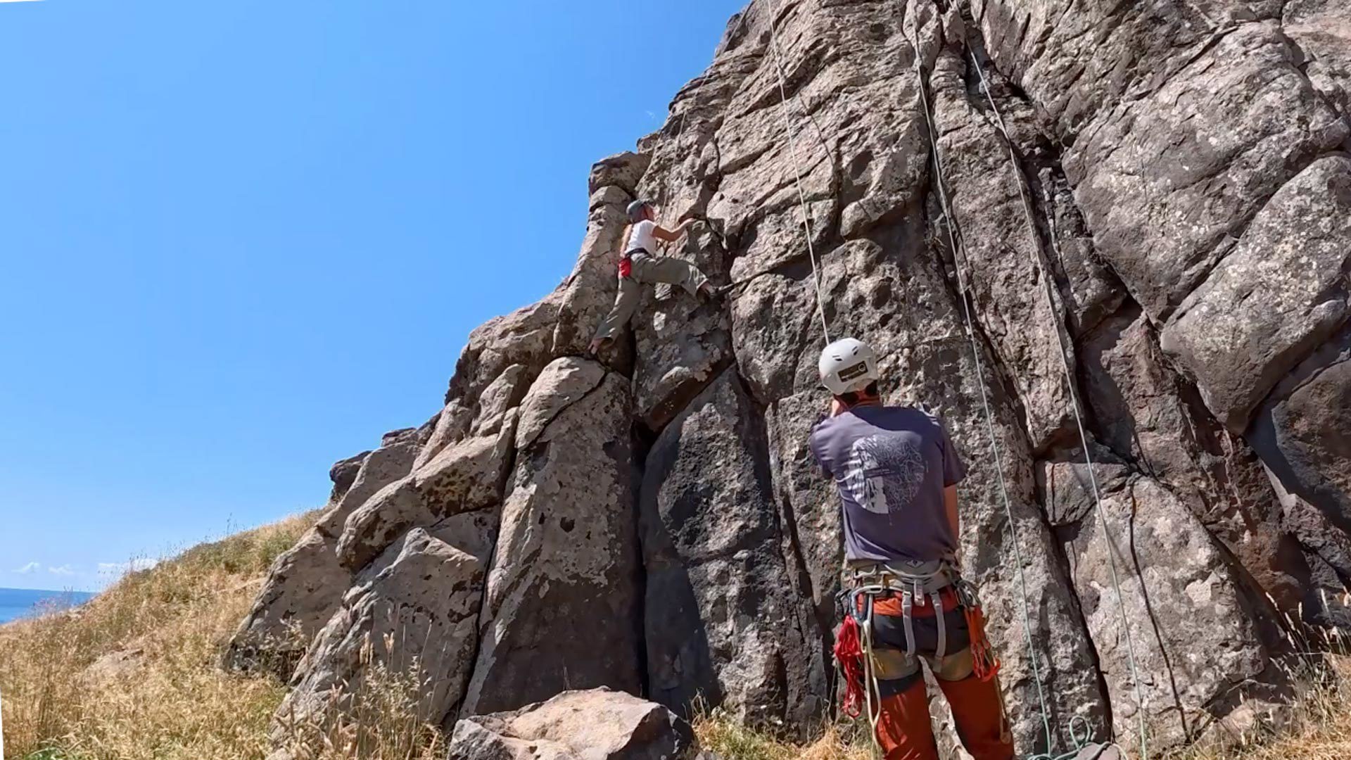 Frau beim Klettern, ausgestattet mit Helm und Gurt.