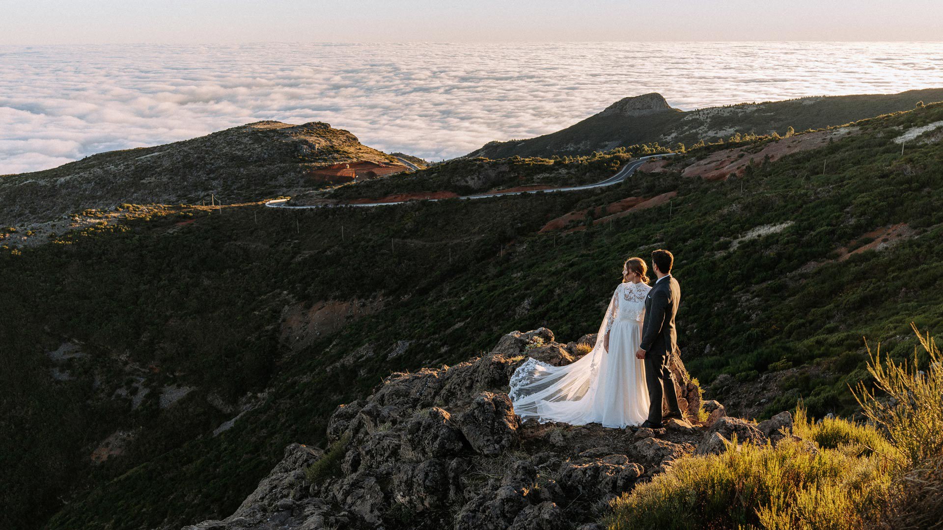 Pareja con atuendos de boda en las montañas, sobre las nubes.