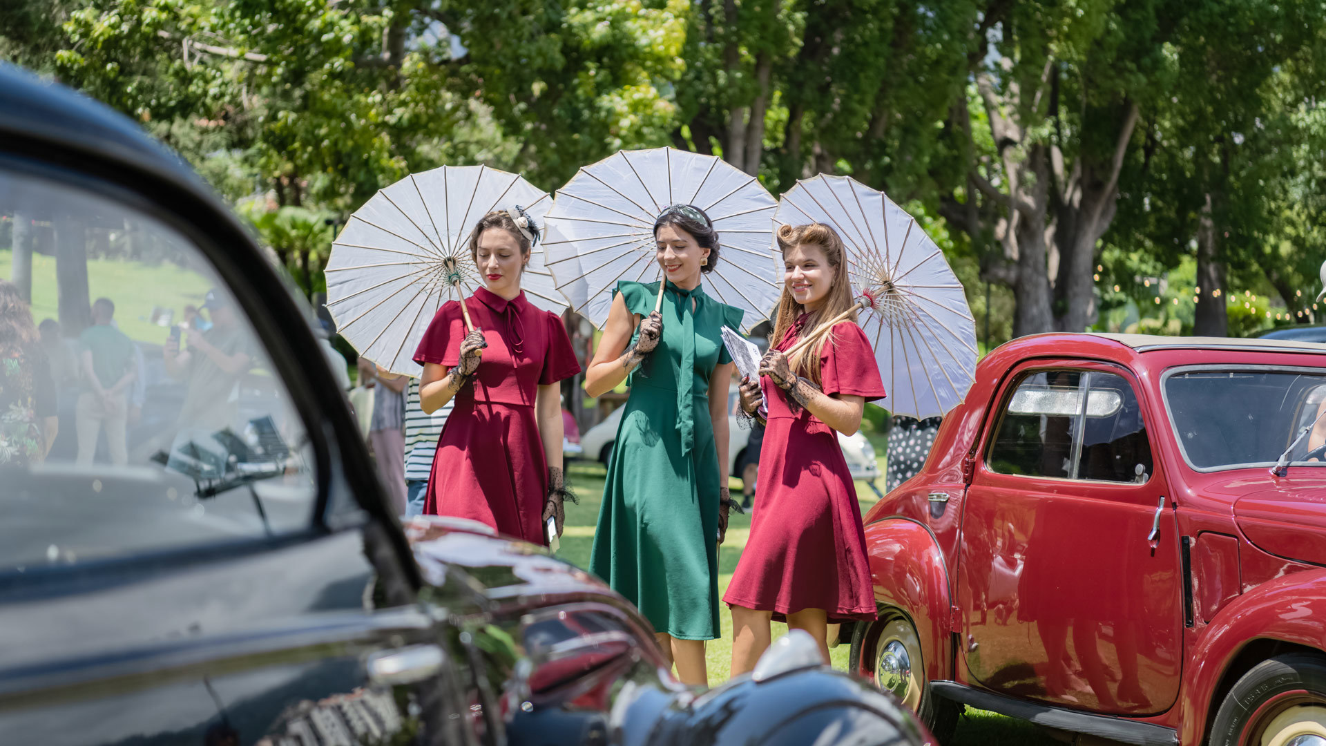 Mujeres con trajes de época junto a un coche clásico en exposición.
