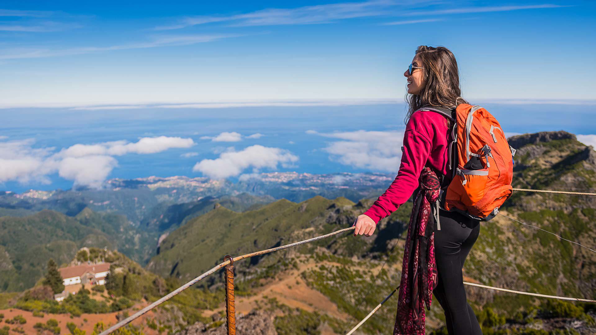 Mujer con chaqueta rosa y mochila naranja en un mirador en Madeira.