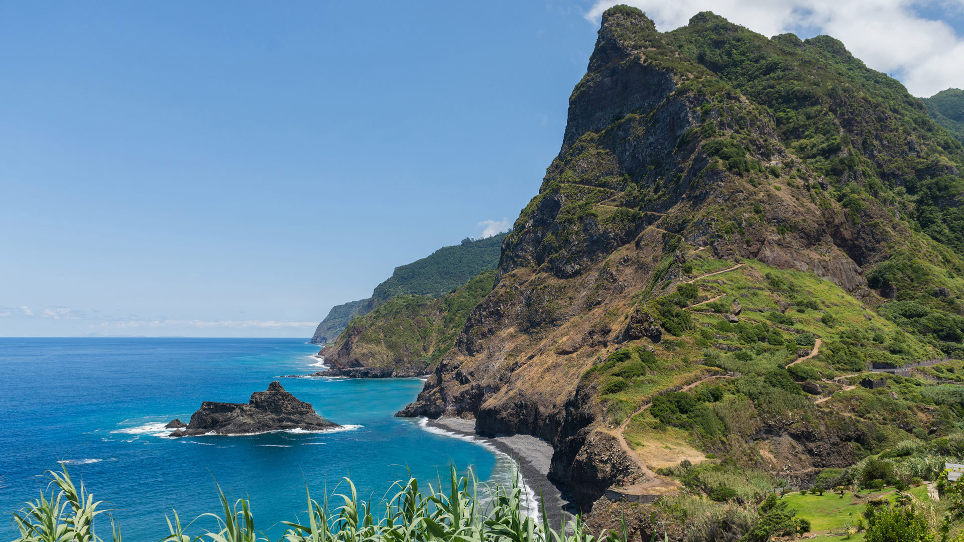 Mer au large d’un versant vert avec chemin visible.