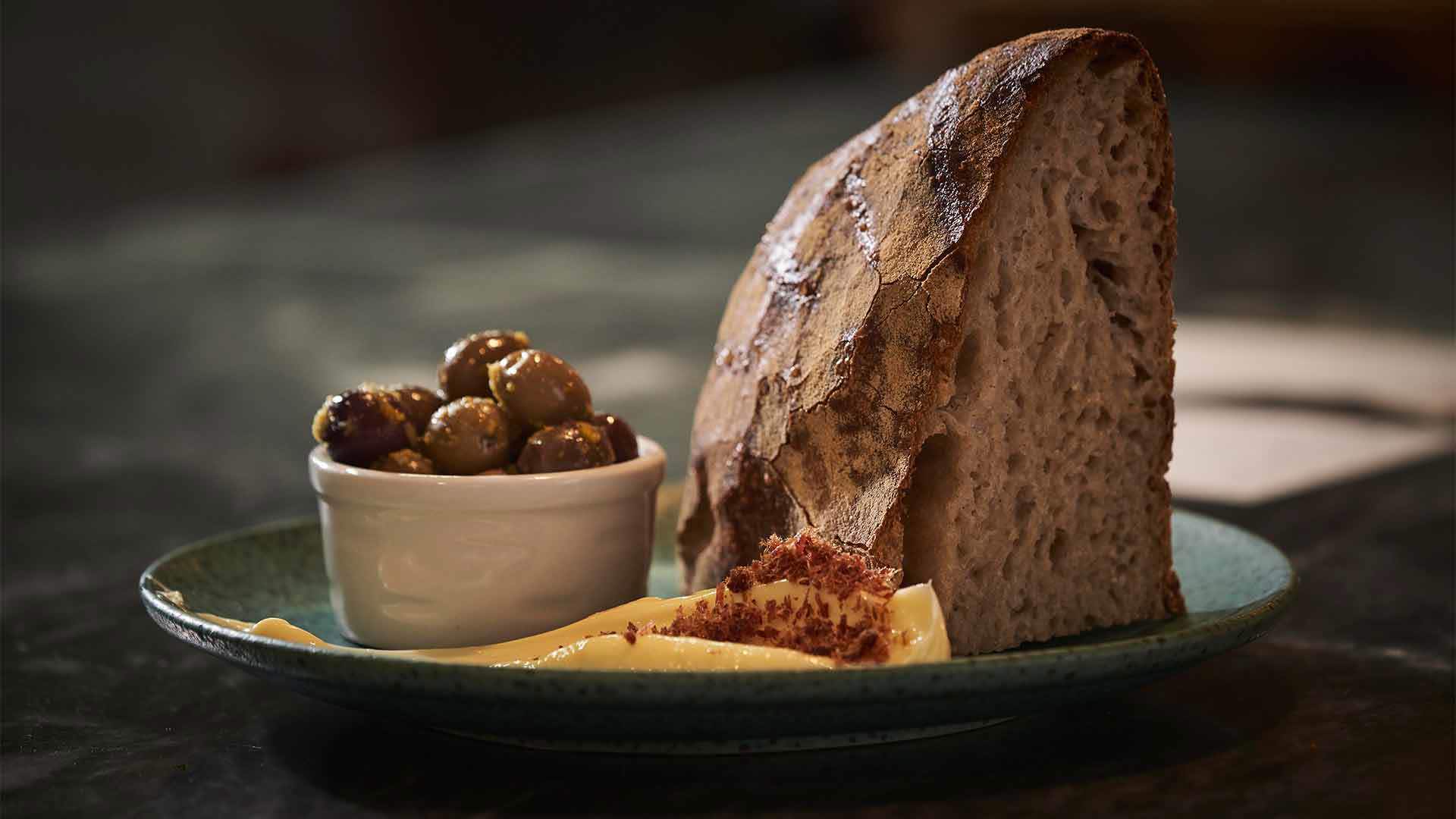 Teller mit Brot, Butter und Oliven in einer kleinen Schale.
