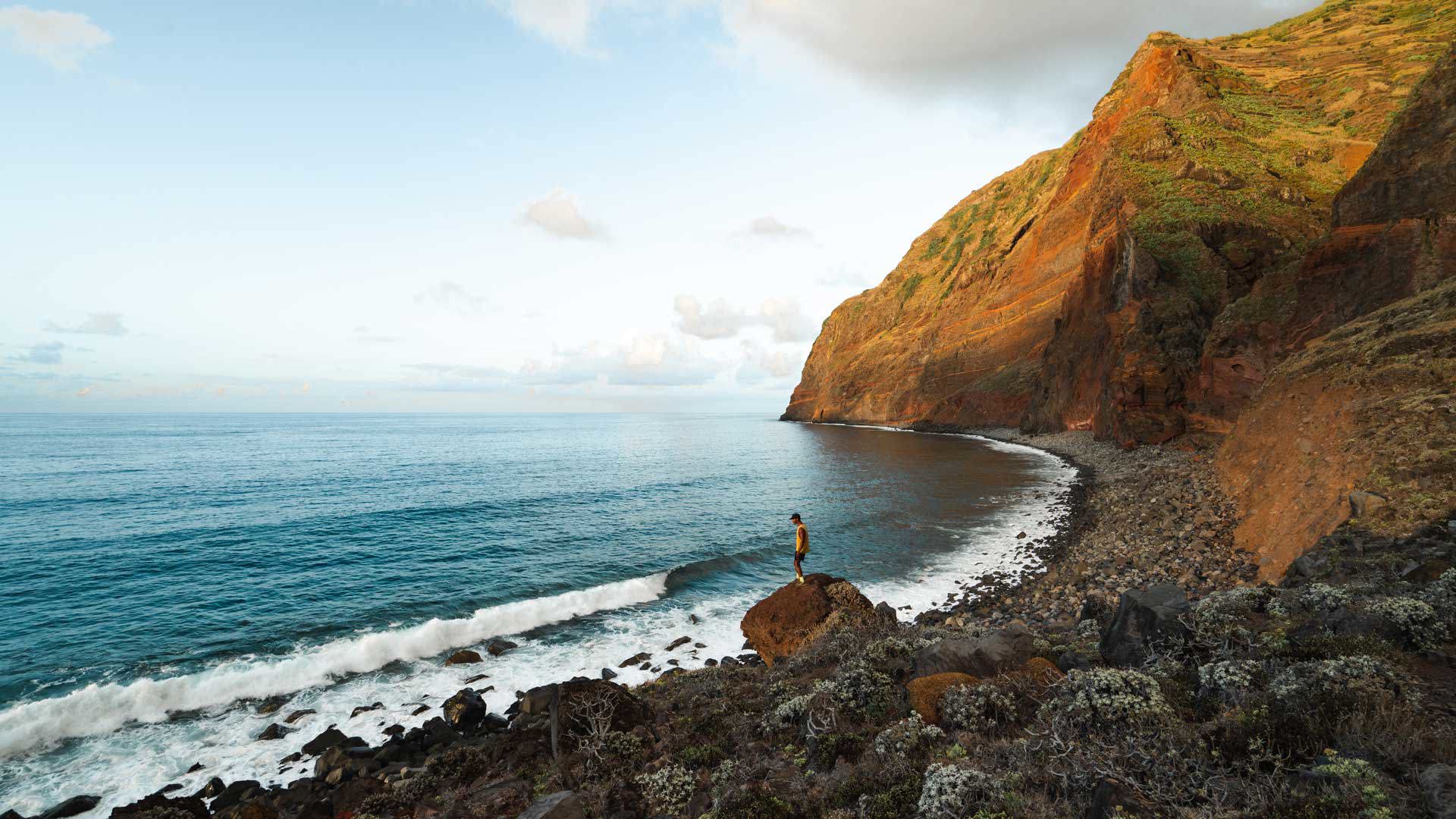 Mann am Meer und Felsen am sonnenbeschienenen Hang auf Madeira.