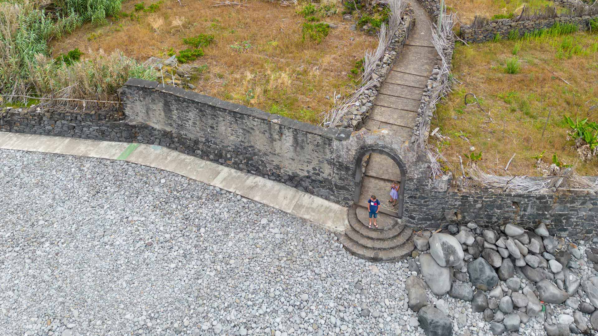 Praia de calhau junto a terrenos com escadas na Madeira.