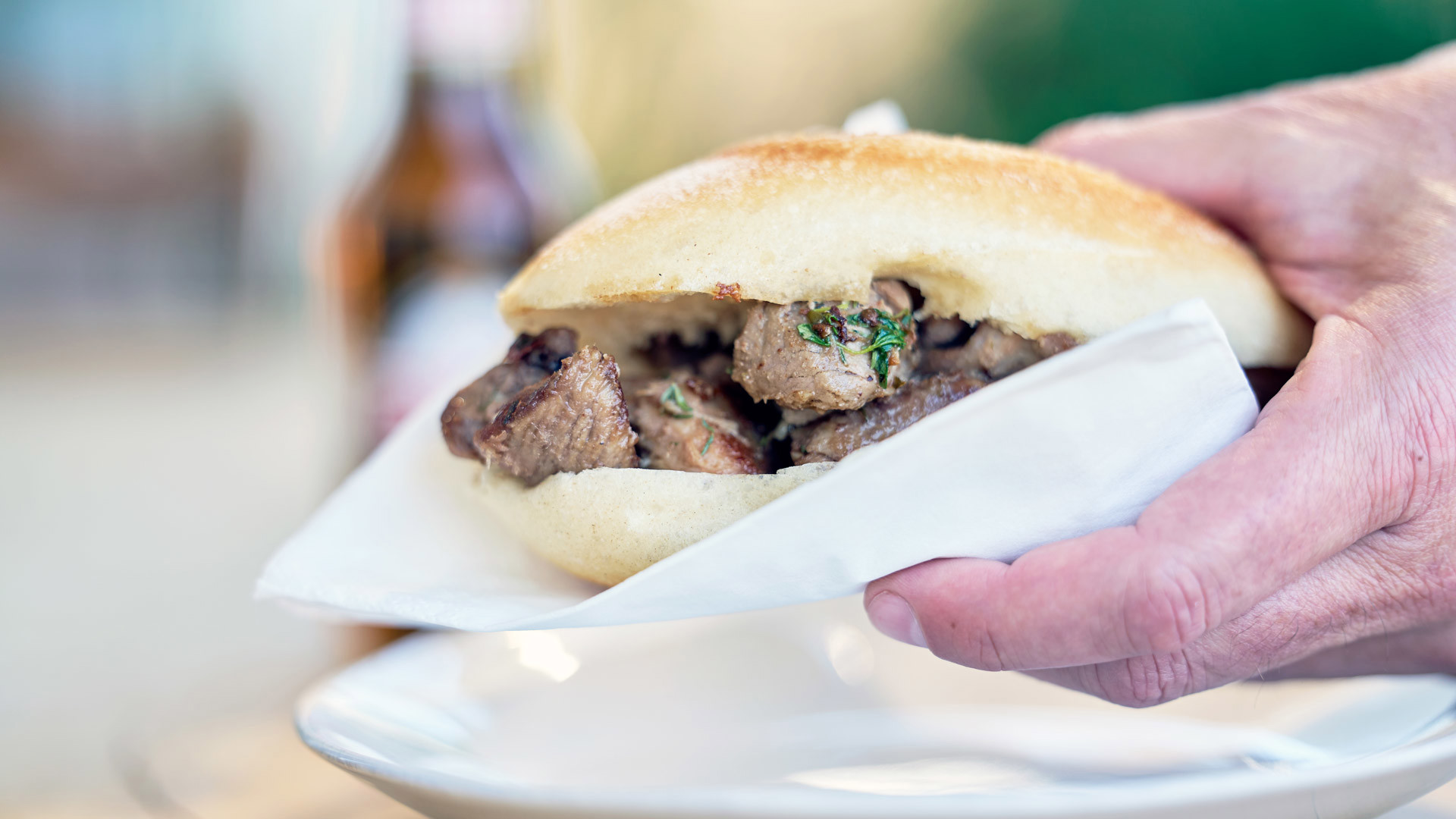 Hand holding a carne de vinho e alhos sandwich, a traditional gastronomic speciality of Madeira Island.