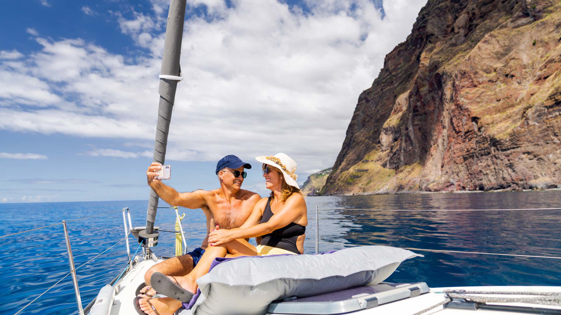 Pareja madura en un barco en el mar con la costa al fondo.