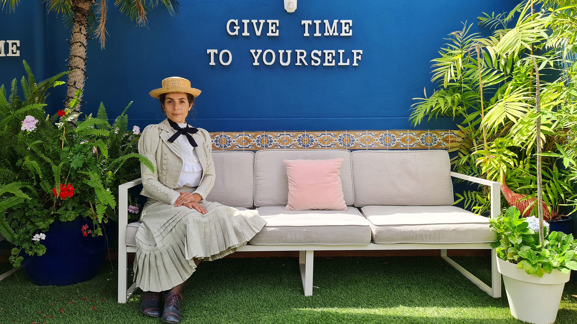 Woman sitting on sofa with plants by a blue wall.