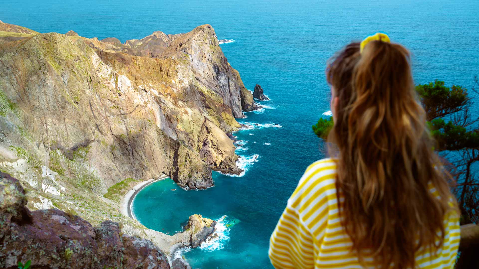 Frau in gelbem Hemd mit weißen Streifen, mit Berg und Meer im Hintergrund.