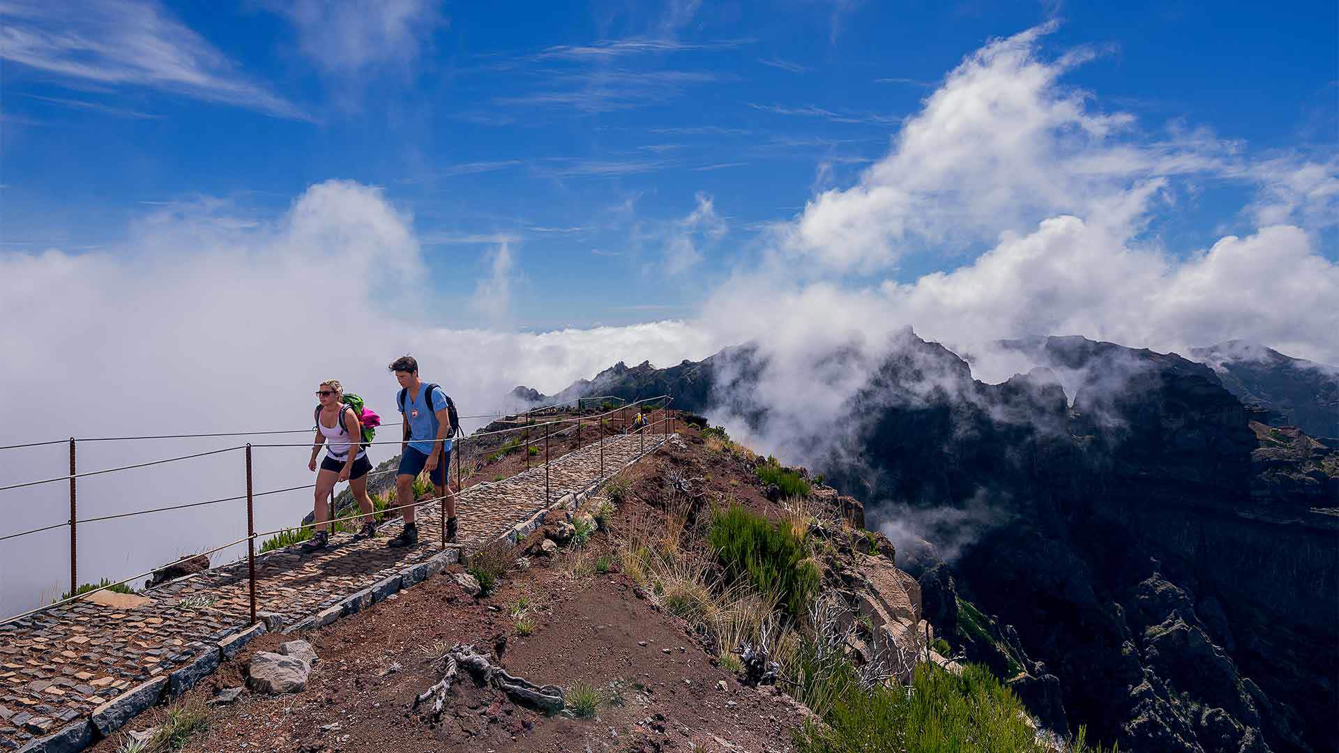 Dos personas caminando por un sendero en la montaña con nubes en Madeira.