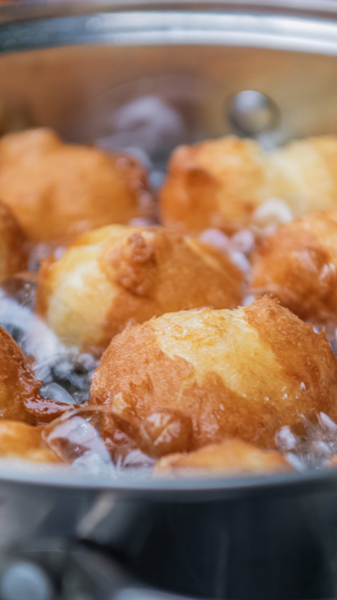 Malassadas werden in einer Pfanne mit heißem Öl frittiert.