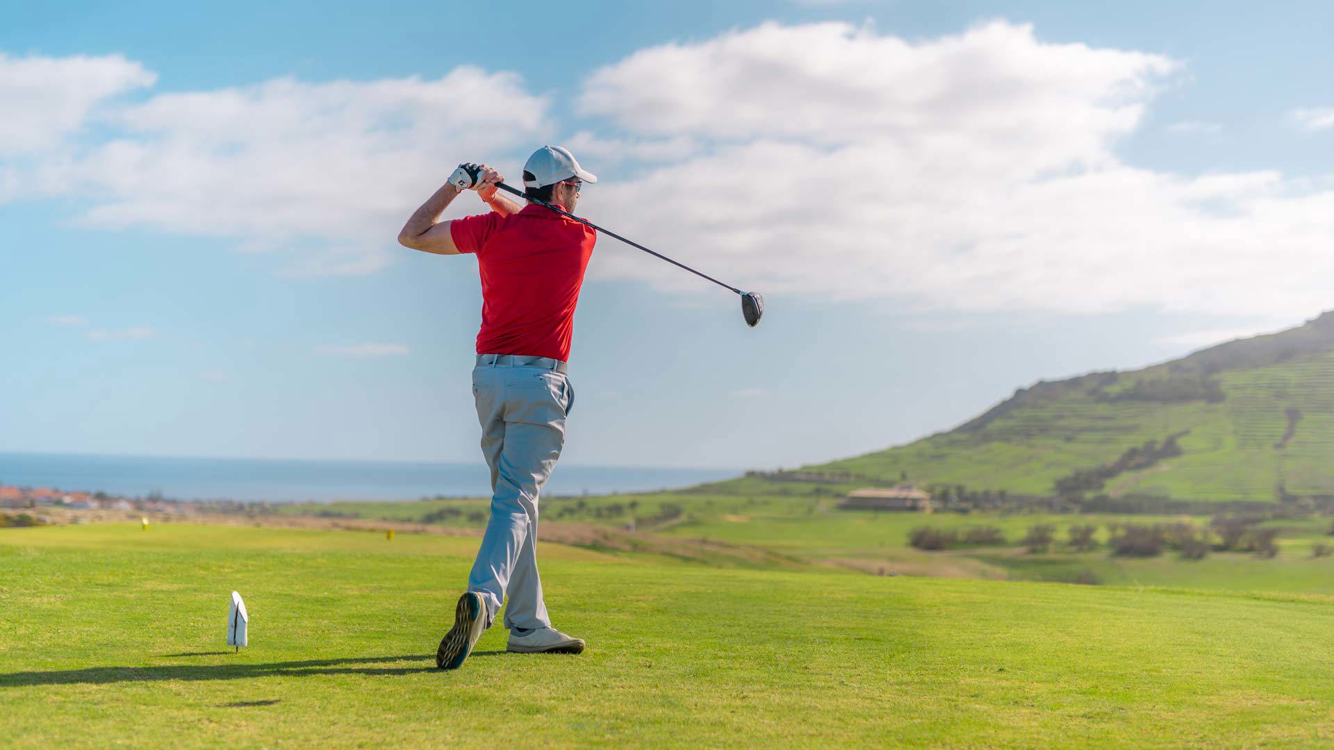 Mann spielt Golf auf einem weiten, grünen Platz.