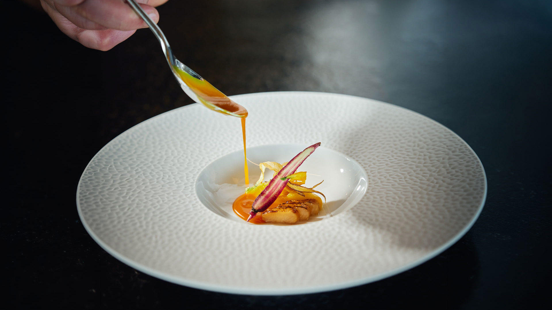 Mano sirviendo un postre con una cuchara en un plato, inspirado en la gastronomía de la isla de Madeira.